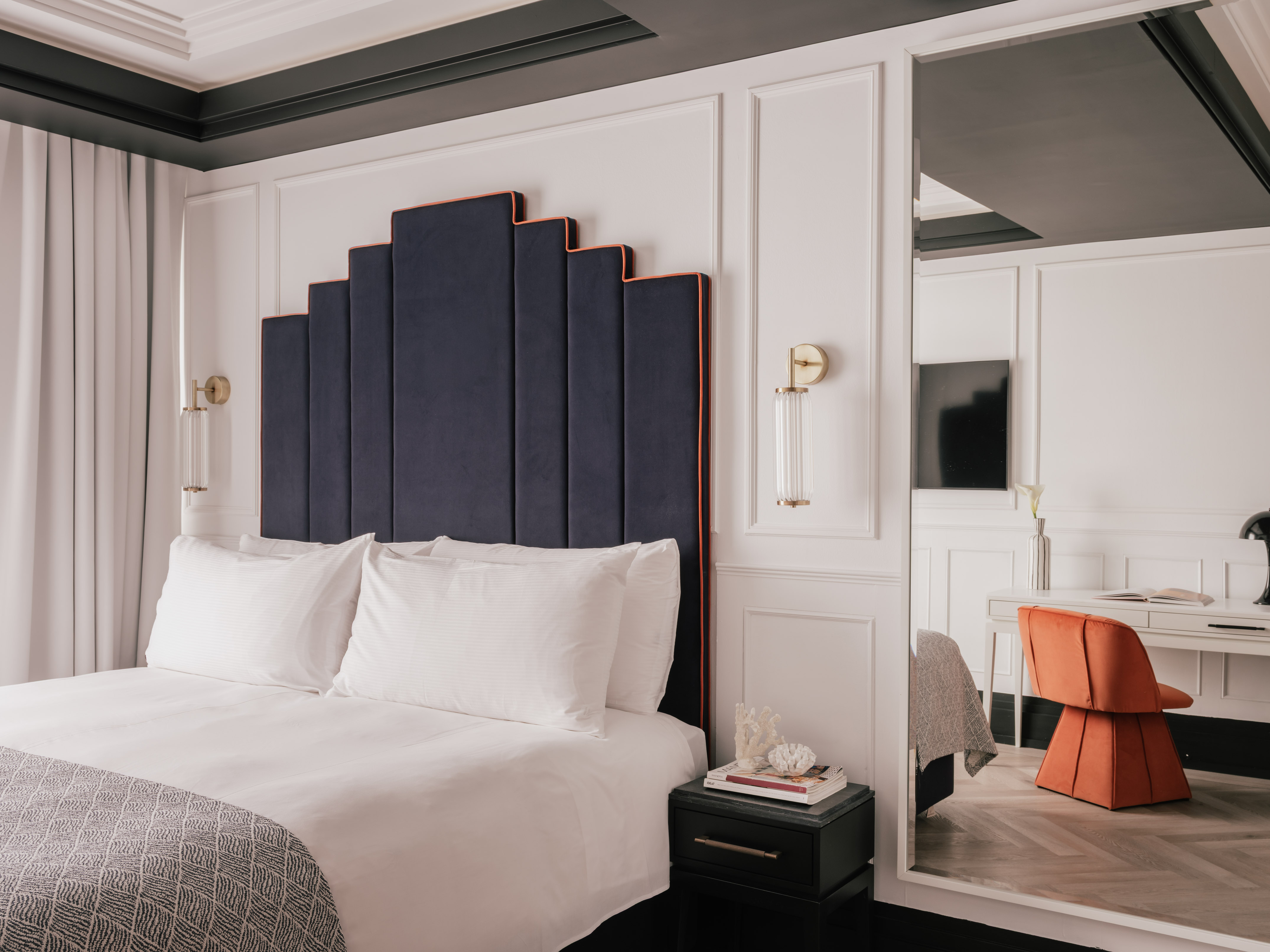 Modern bedroom with navy Art Deco headboard and orange chair.