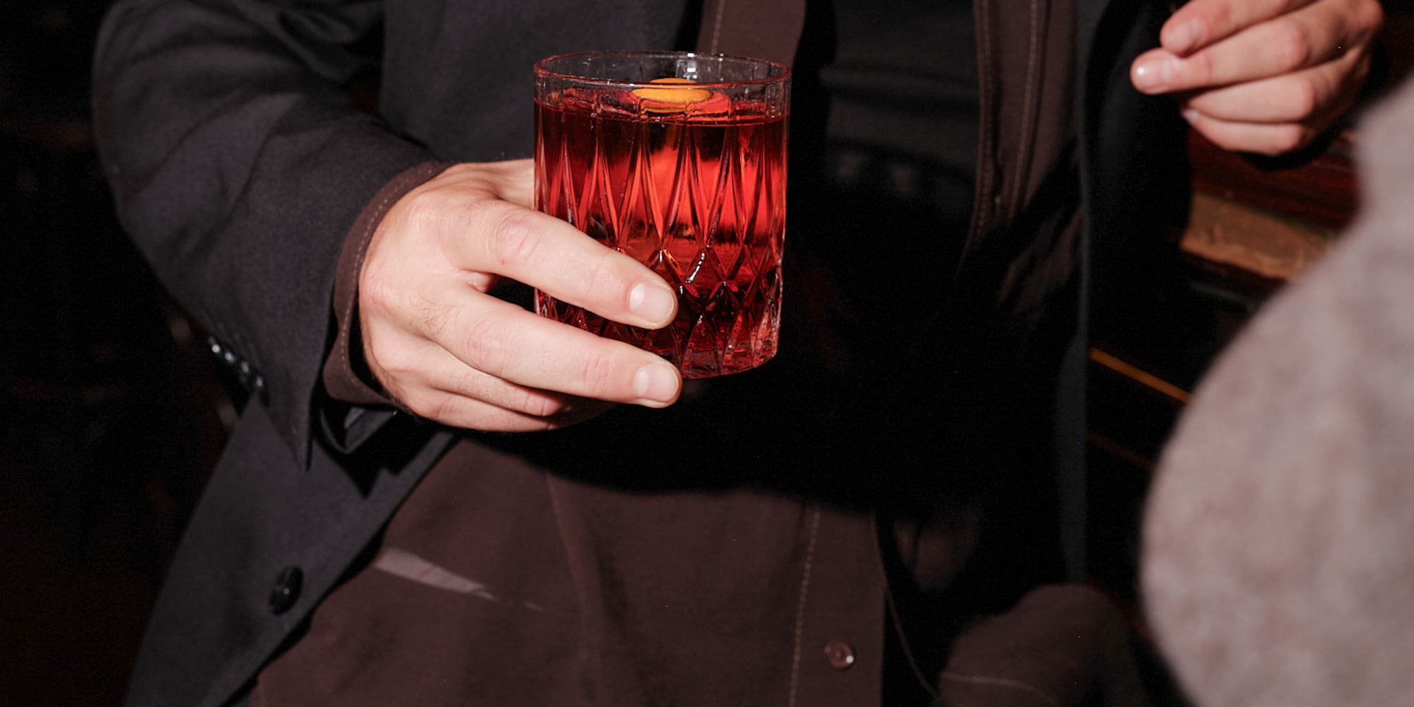 Man holding Negroni cocktail in a patterned glass at a bar.