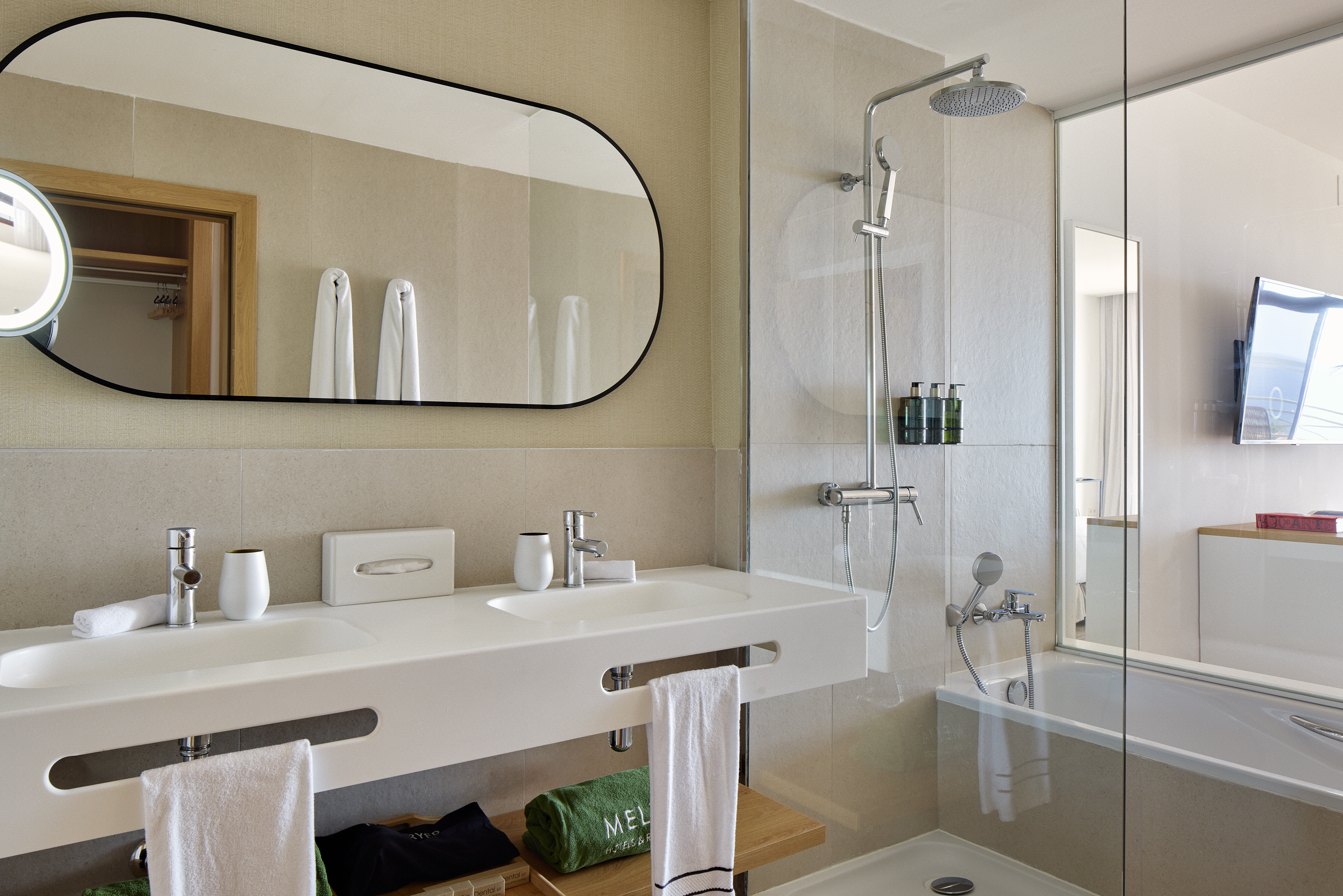 Modern hotel bathroom with double vanity, mirror, glass shower, and tub.