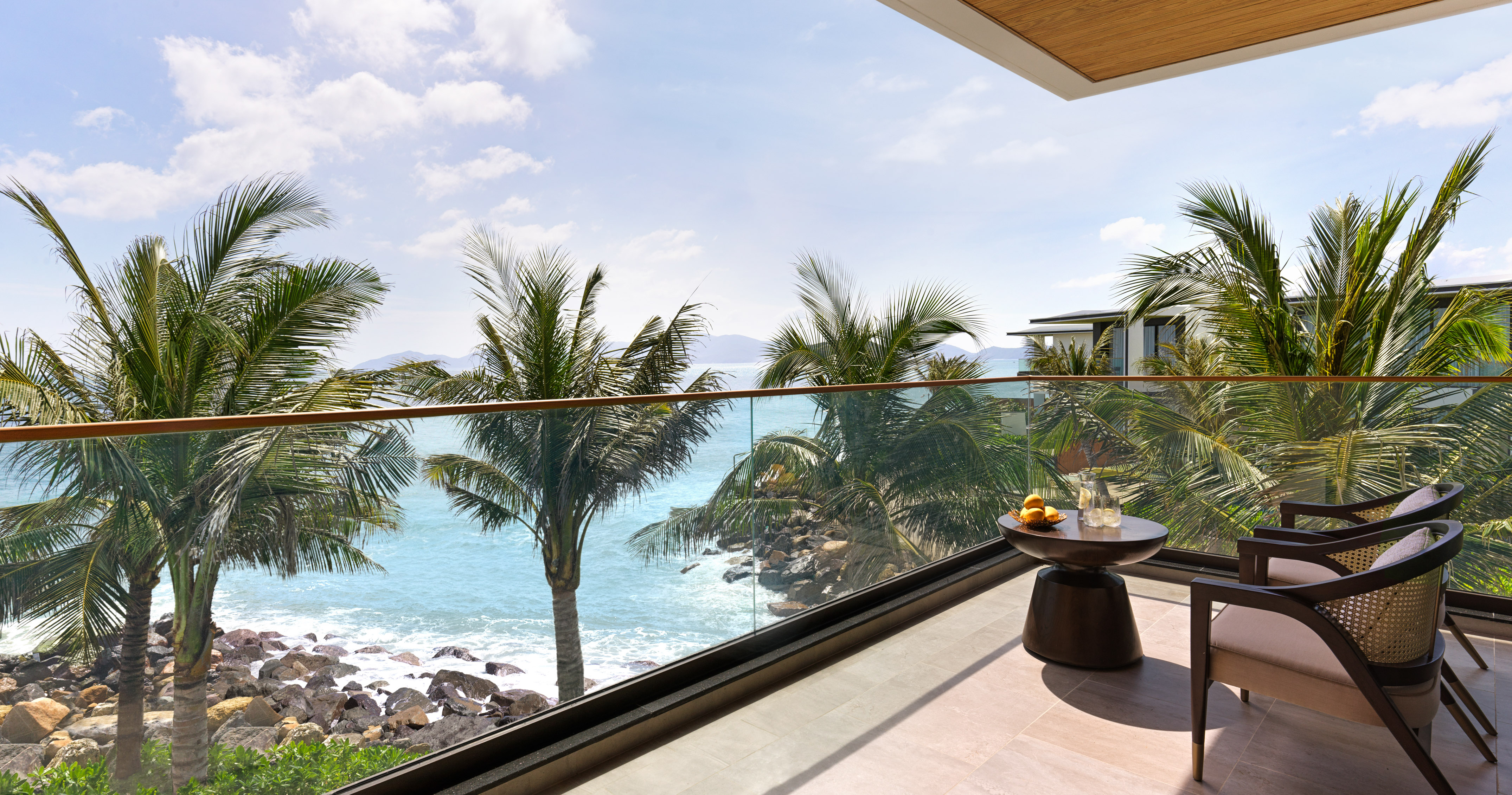 Oceanfront balcony view with palm trees, blue sea, and outdoor seating.