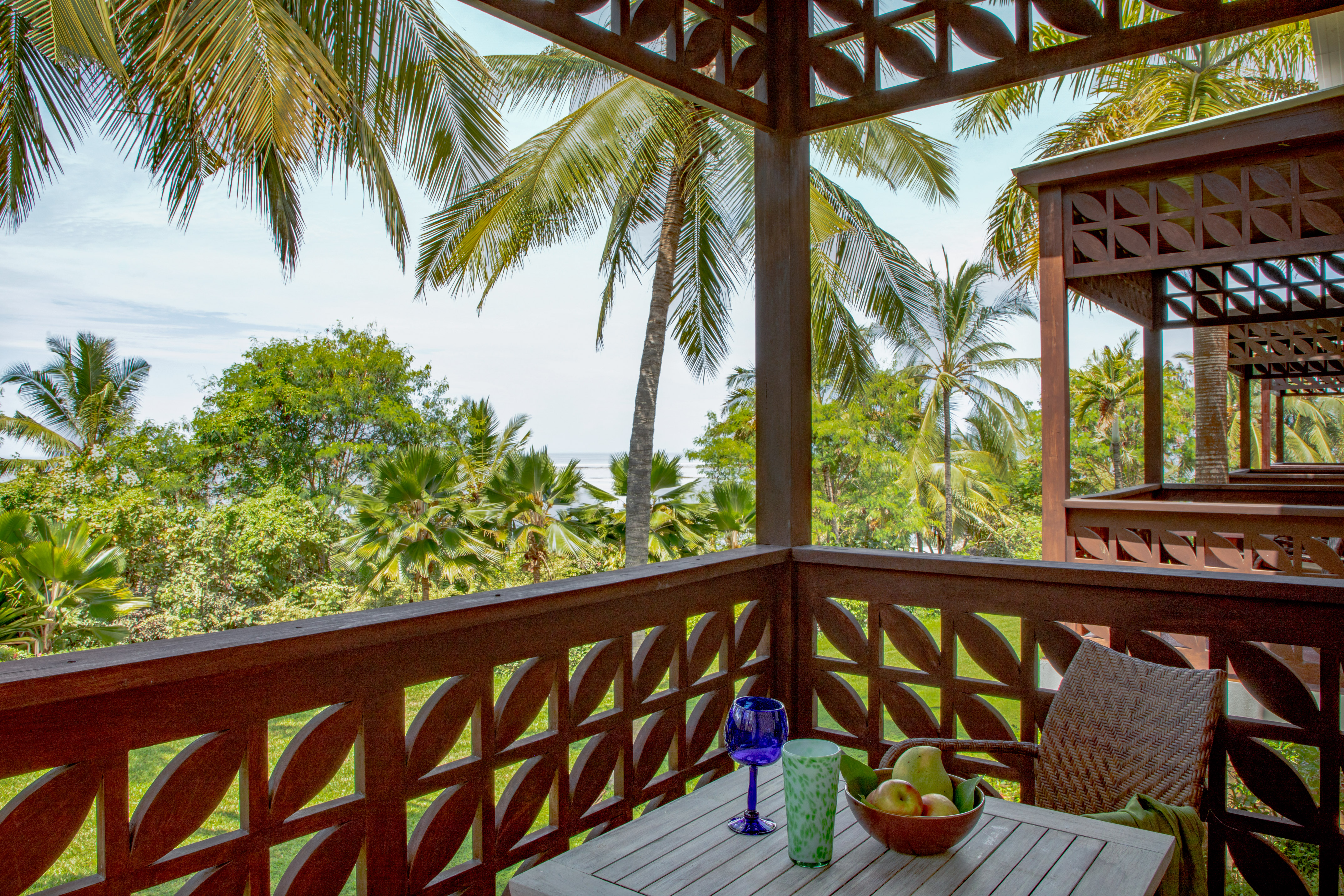 Balcony with ocean view, tropical palm trees, fruit bowl, and wooden decor.