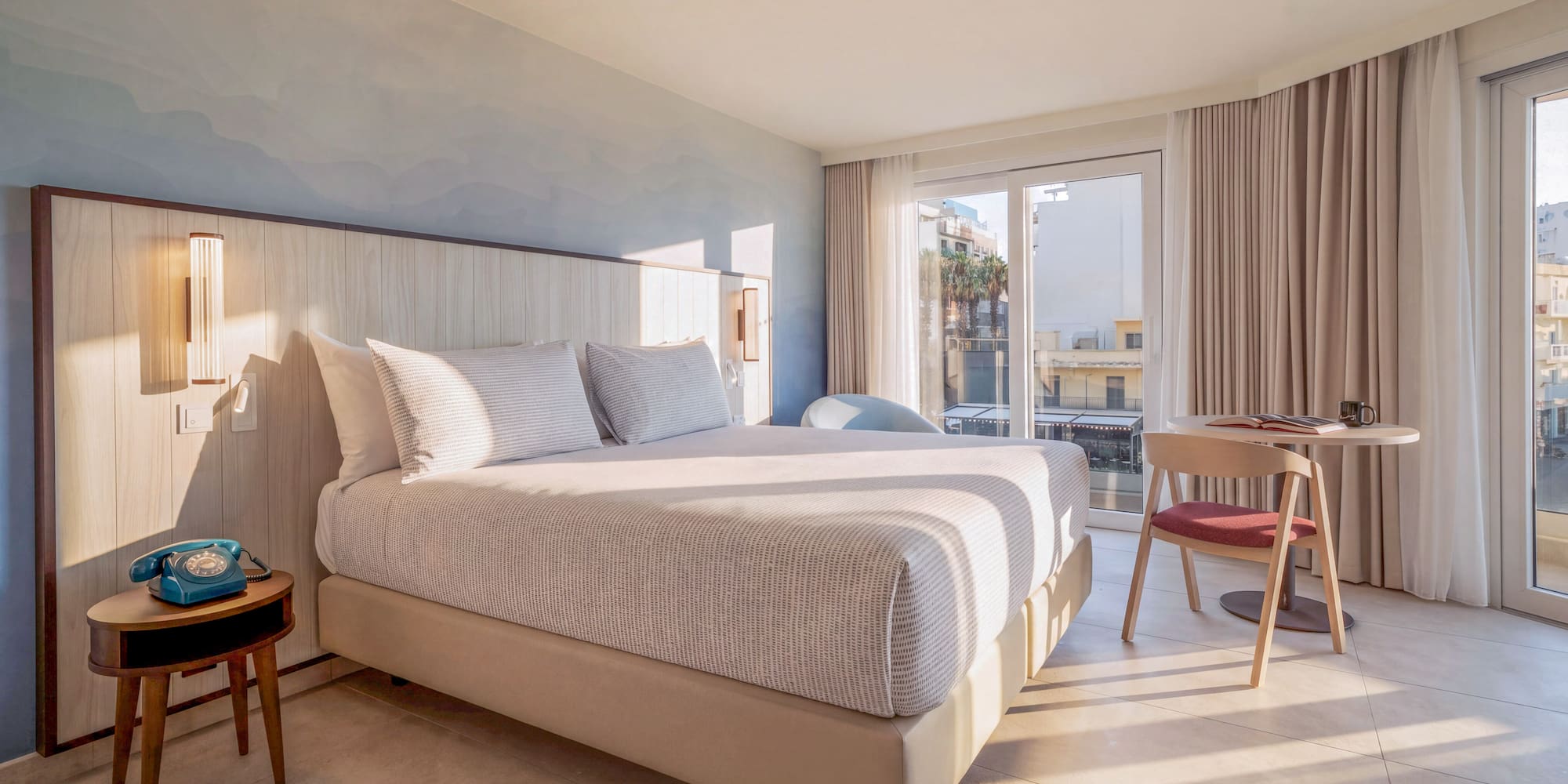 Sunlit modern hotel room with large bed, wooden headboard, and balcony view.