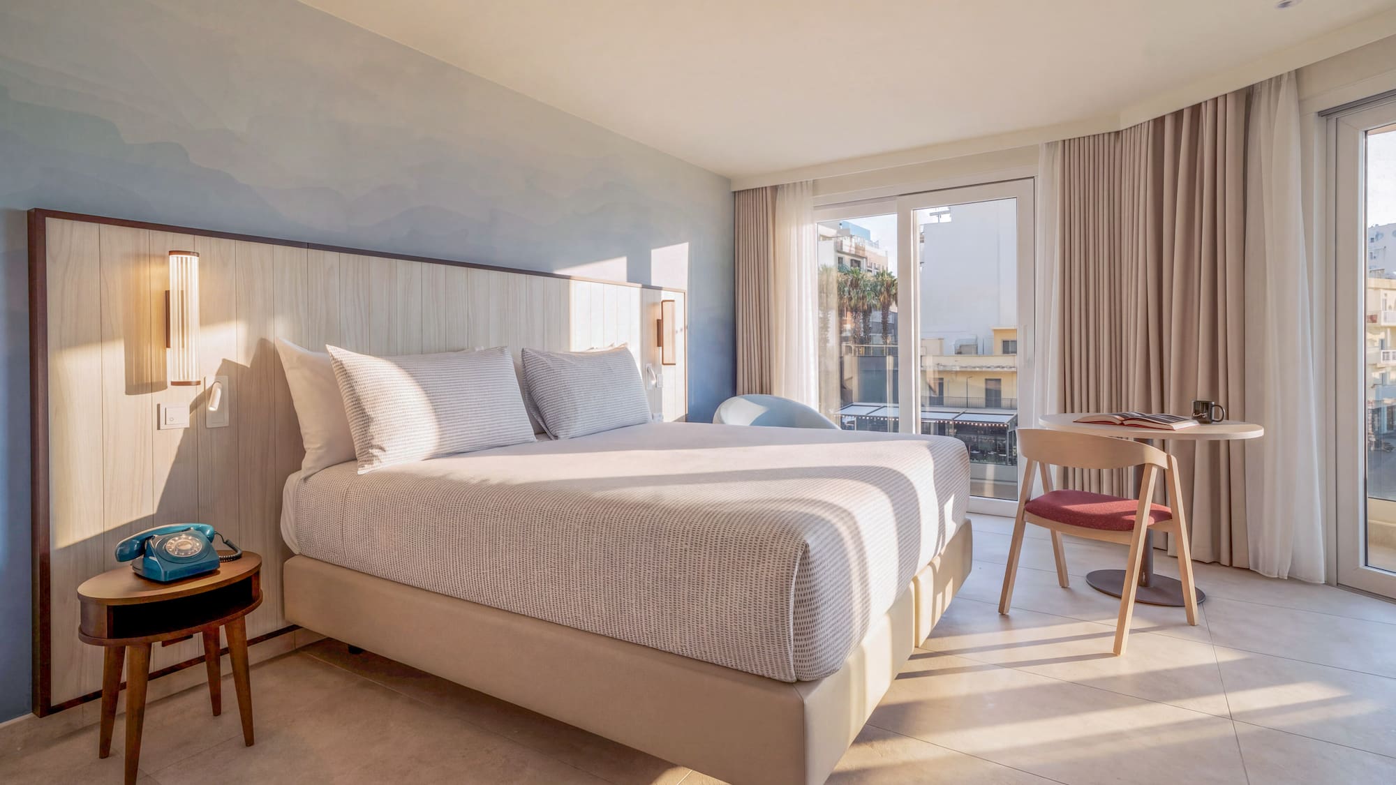 Sunlit modern hotel room with large bed, wooden headboard, and balcony view.
