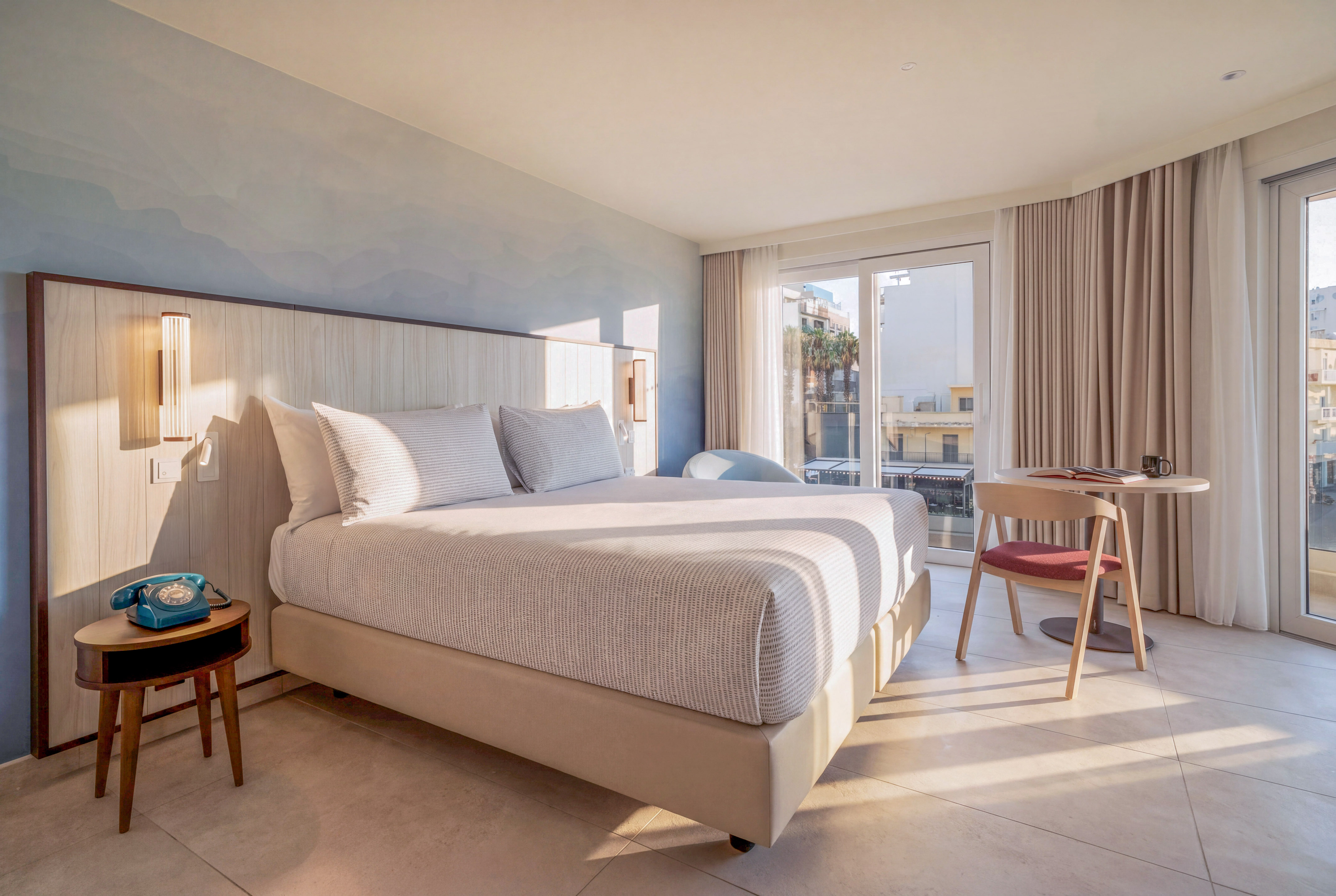 Sunlit modern hotel room with large bed, wooden headboard, and balcony view.
