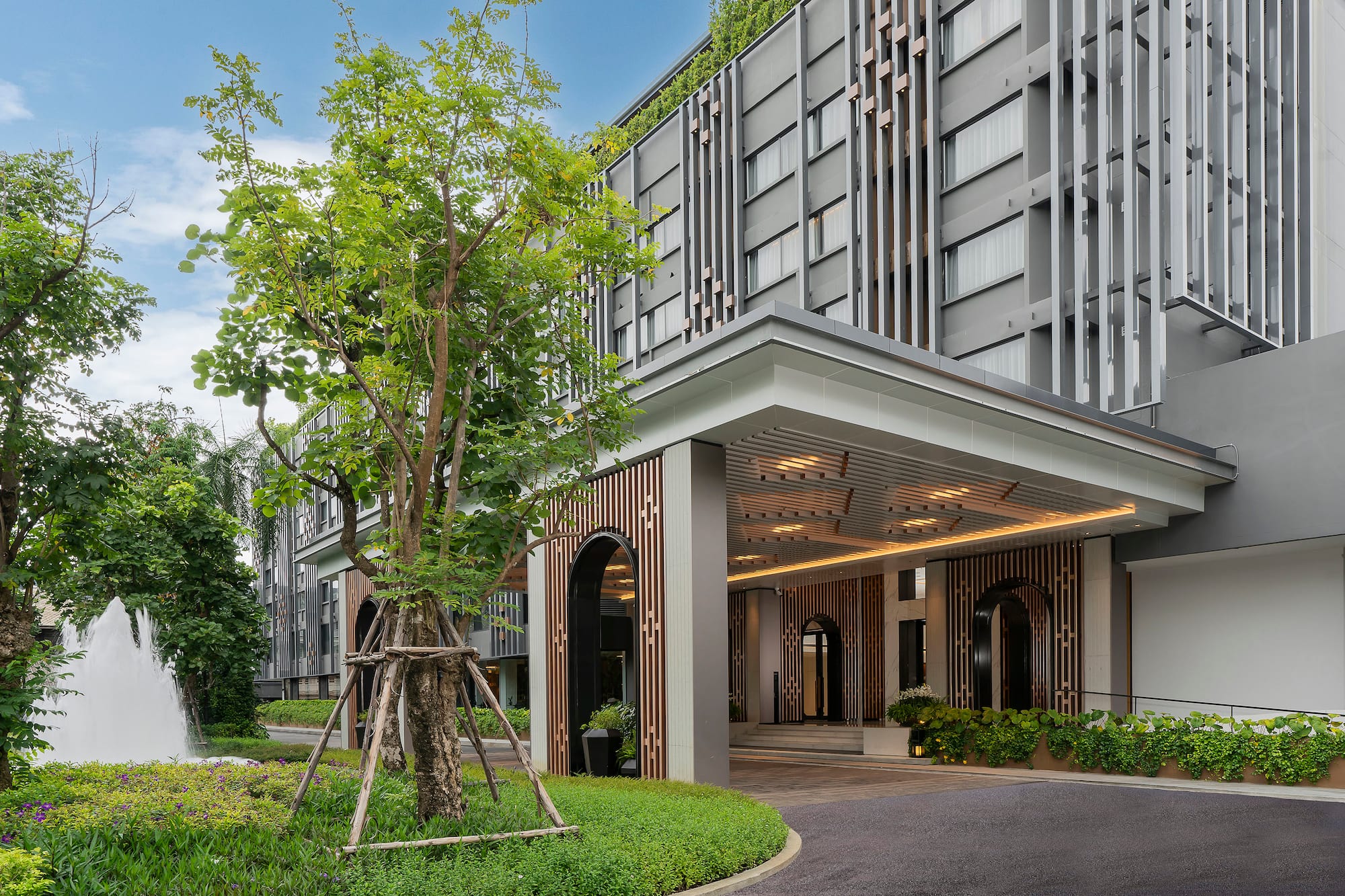 Modern resort entrance with lush green garden, a fountain, and elegant facade.