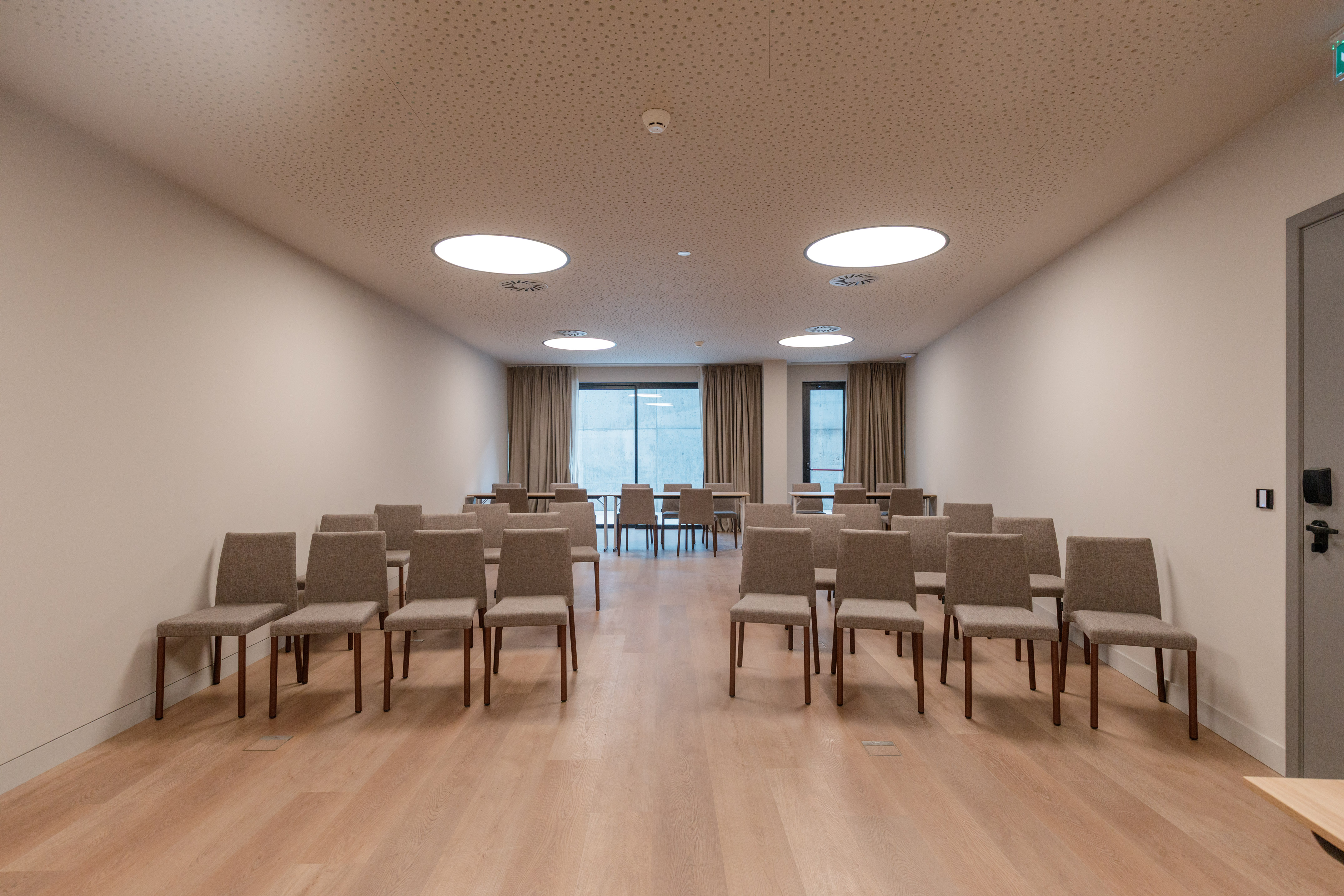 Empty modern conference room with chairs, wood floor, bright ceiling lights.