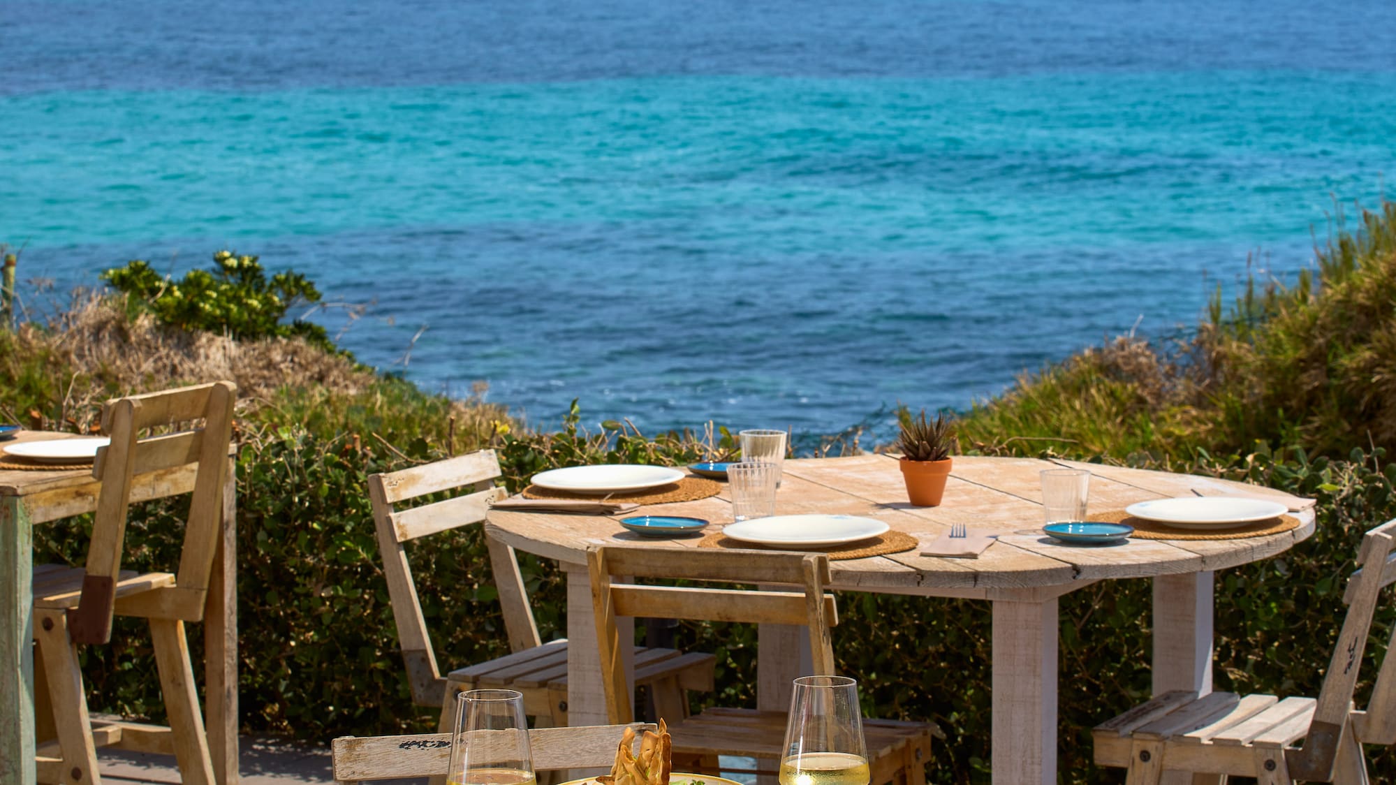 a table and chairs with plates of food on it and a body of water in the background