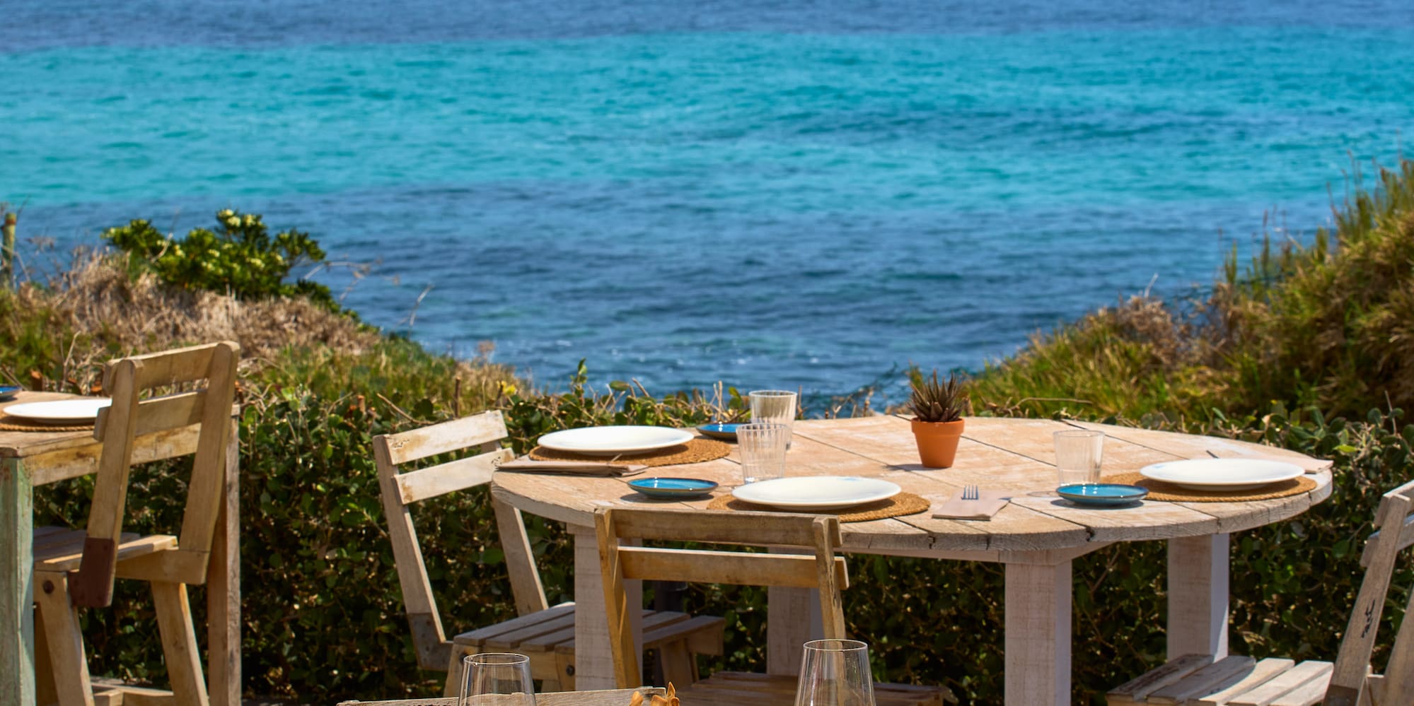a table and chairs with plates of food on it and a body of water in the background
