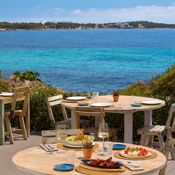 a table and chairs with plates of food on it and a body of water in the background