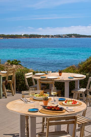 a table and chairs with plates and food on it by the water