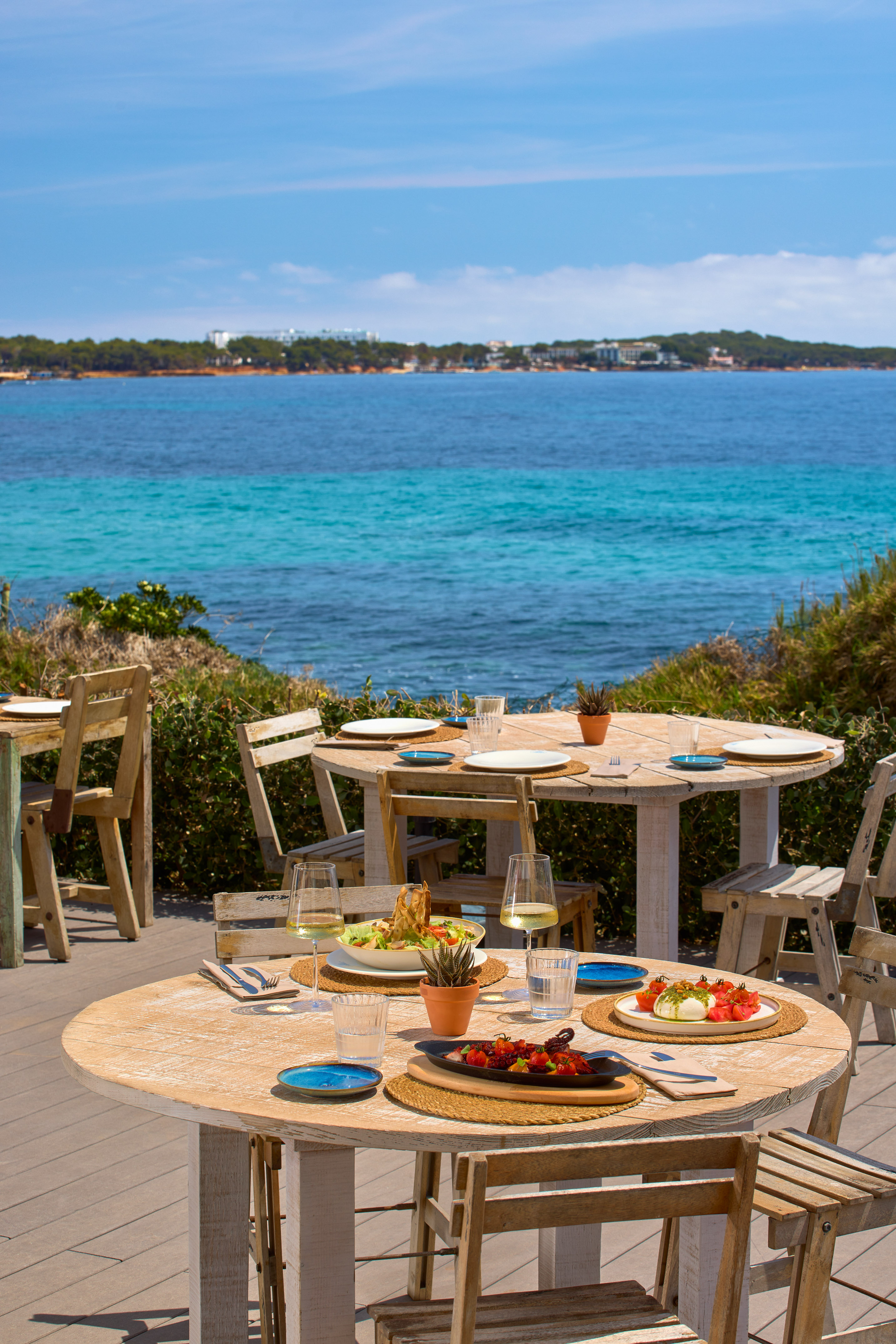 a table and chairs with plates of food on it and a body of water in the background