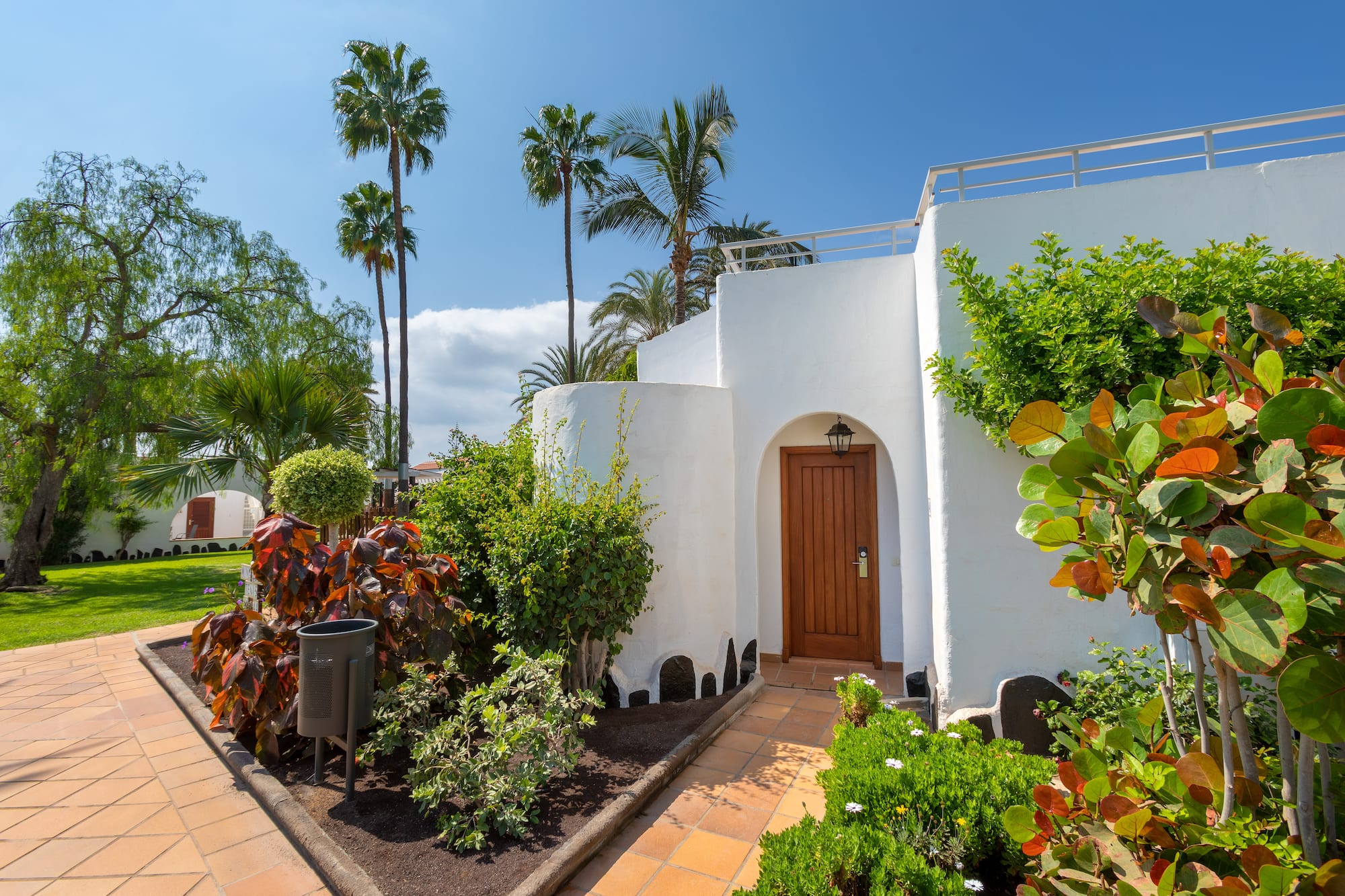 White resort villa entrance, wooden door, tropical garden, palm trees.