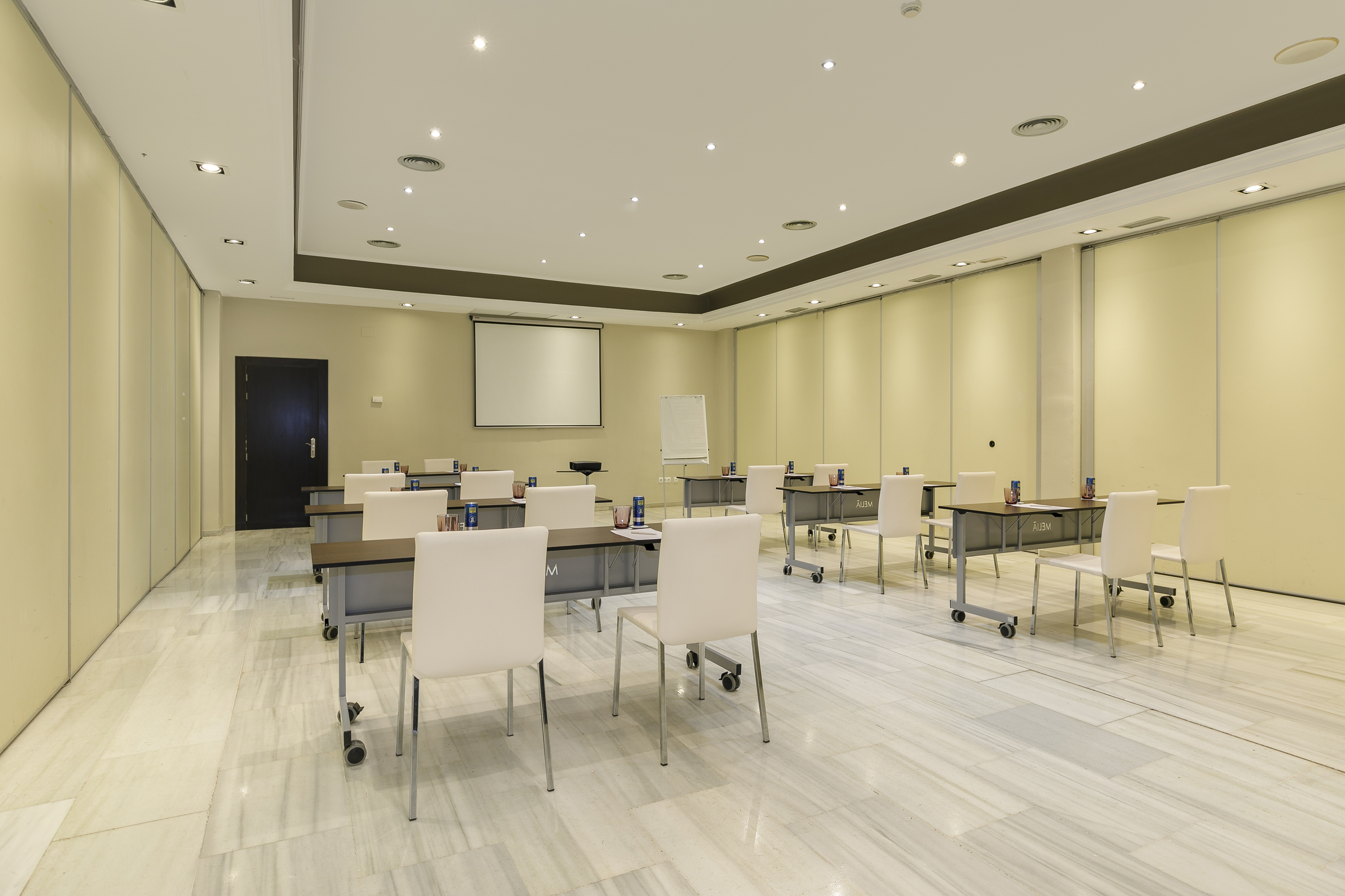 Modern training room with tables, chairs, projector screen, marble floor.