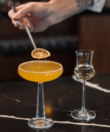a person holding a lemon over a glass of liquid