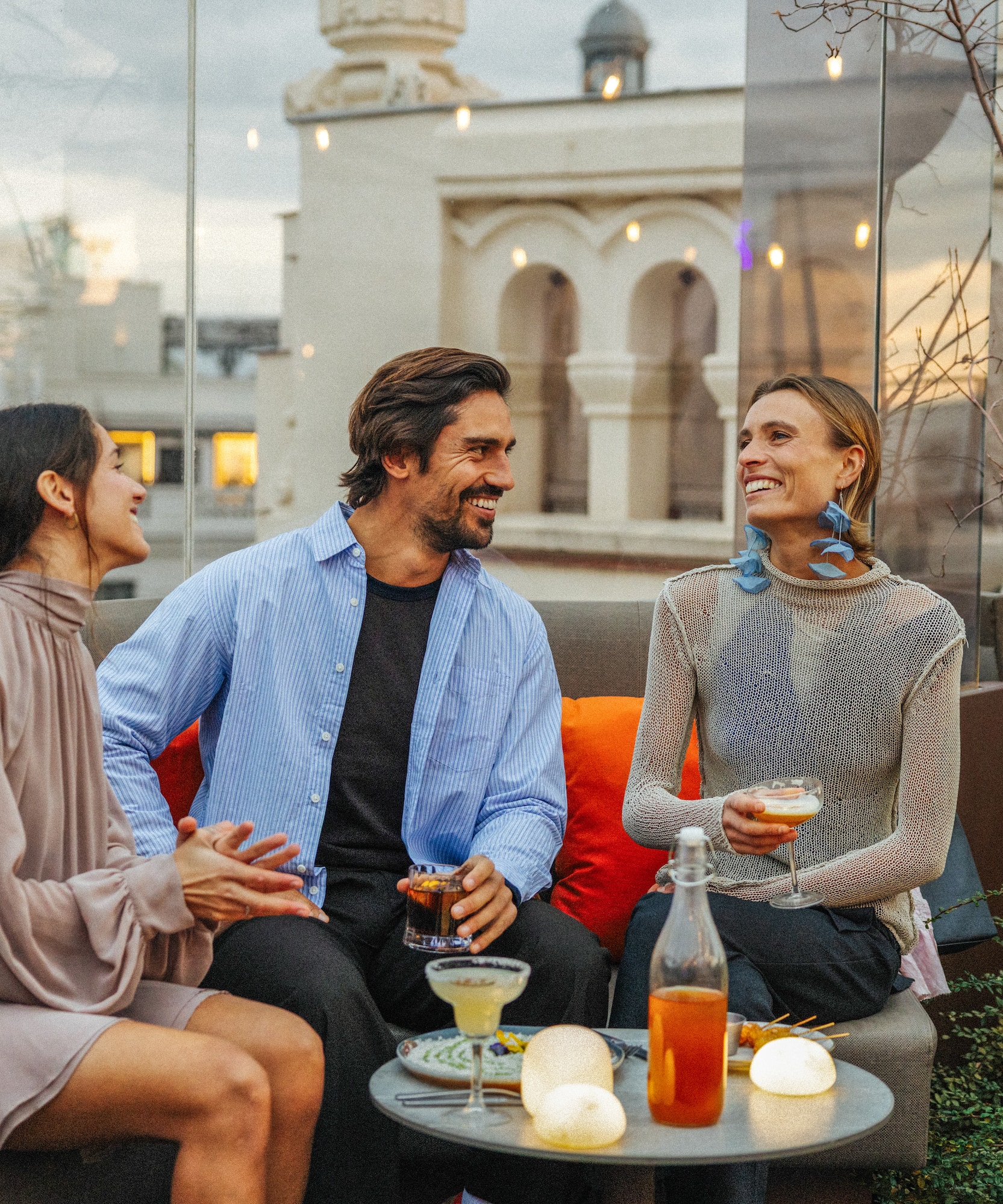 Friends enjoying cocktails at a rooftop bar terrace with city views.