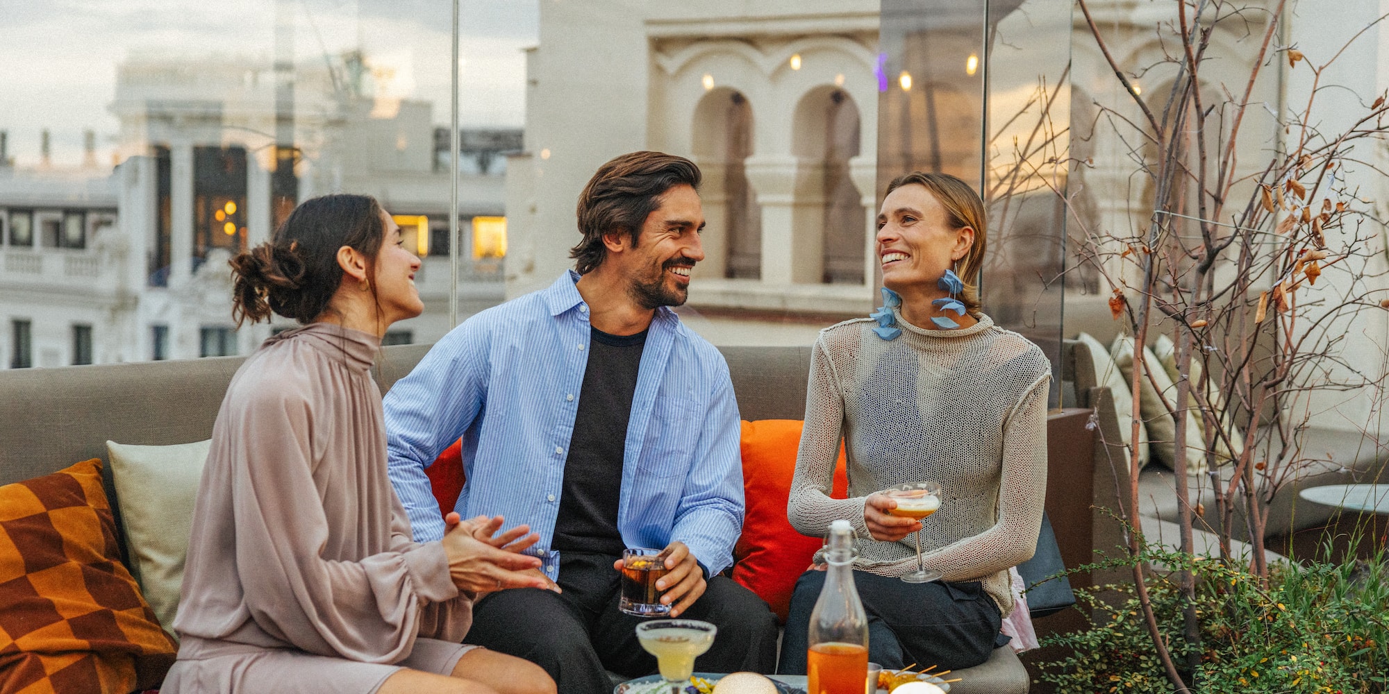 Friends laughing, drinking cocktails on a stylish city rooftop bar.