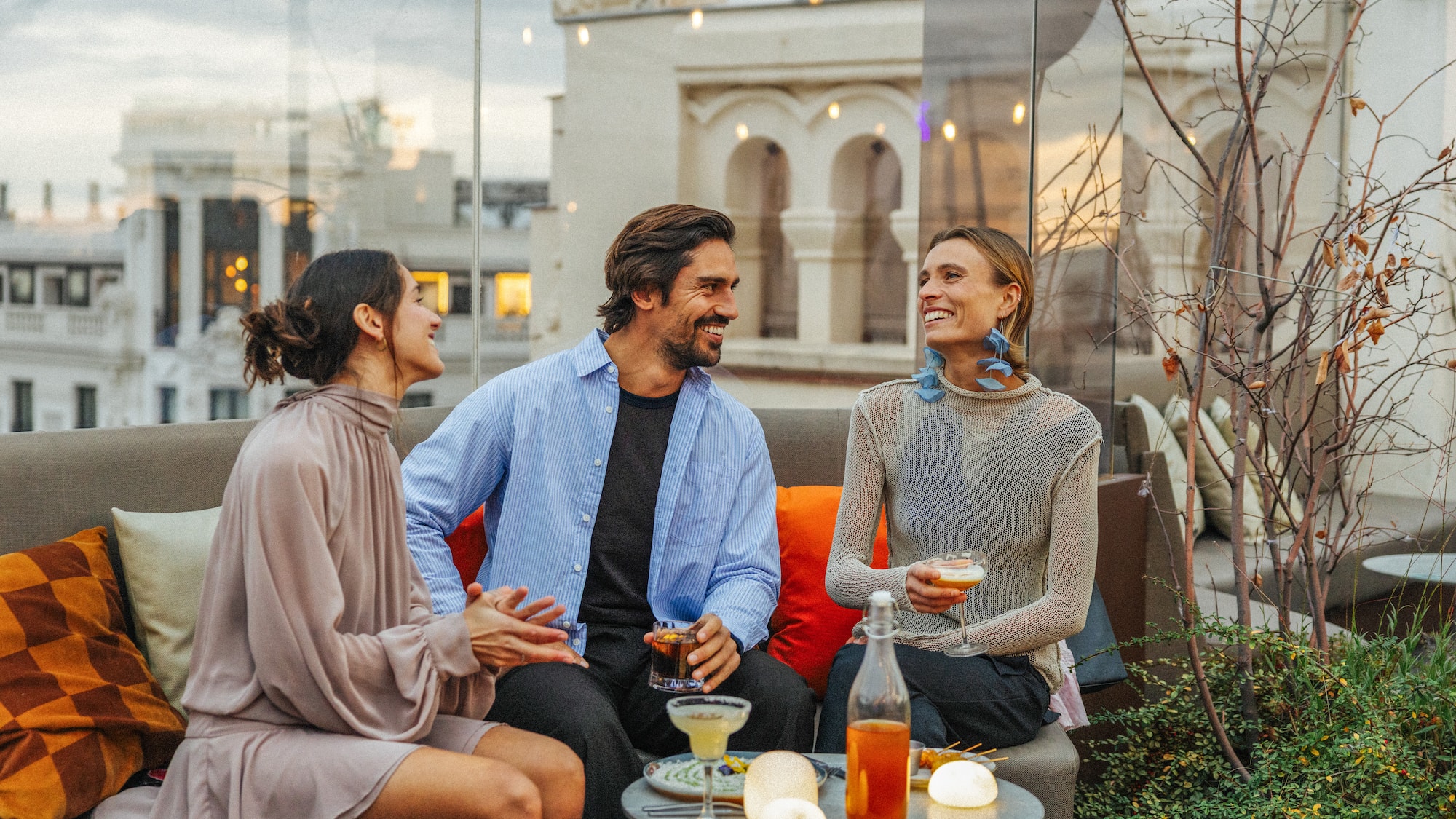 Friends laughing, drinking cocktails on a stylish city rooftop bar.