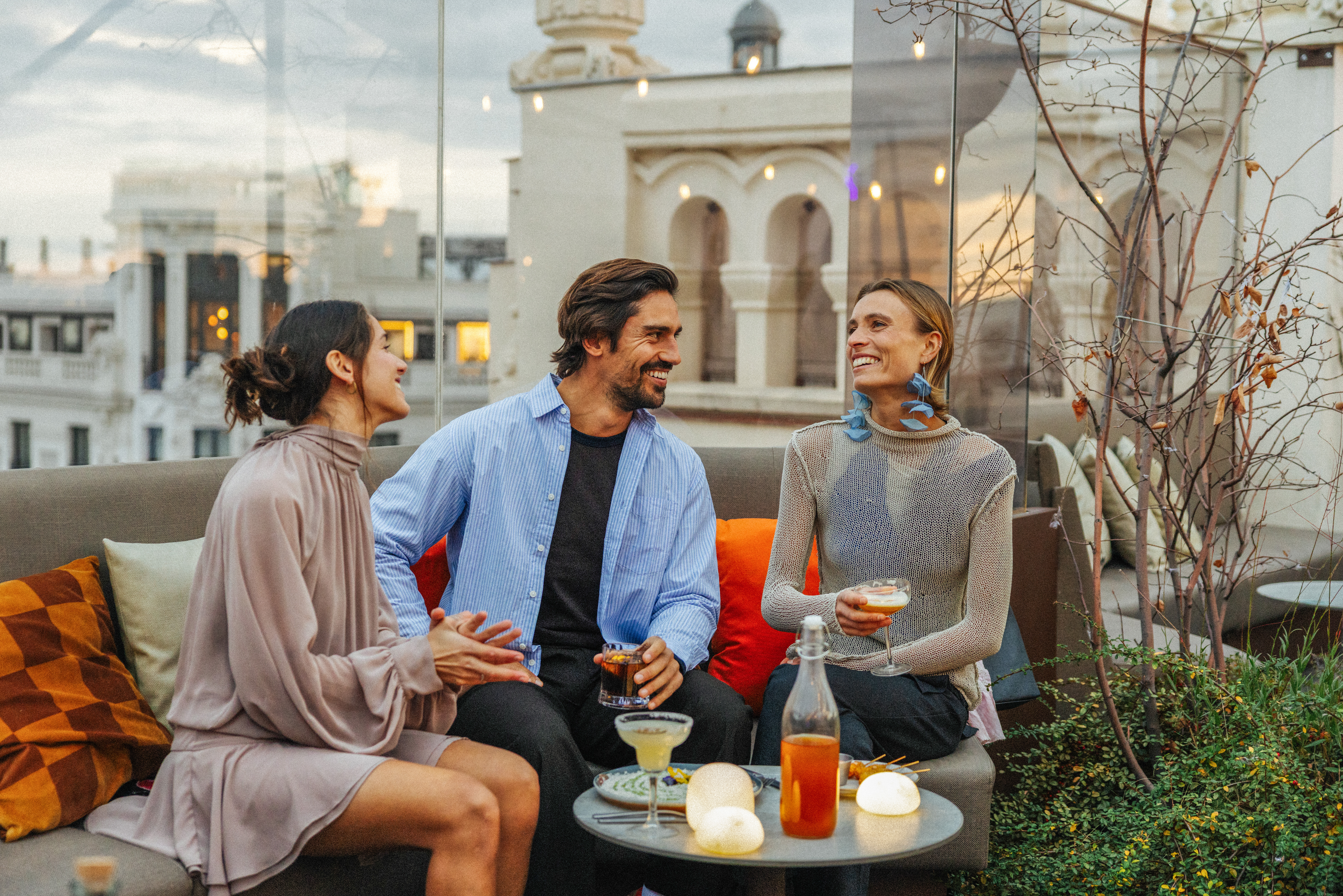 Friends laughing, drinking cocktails on a stylish city rooftop bar.