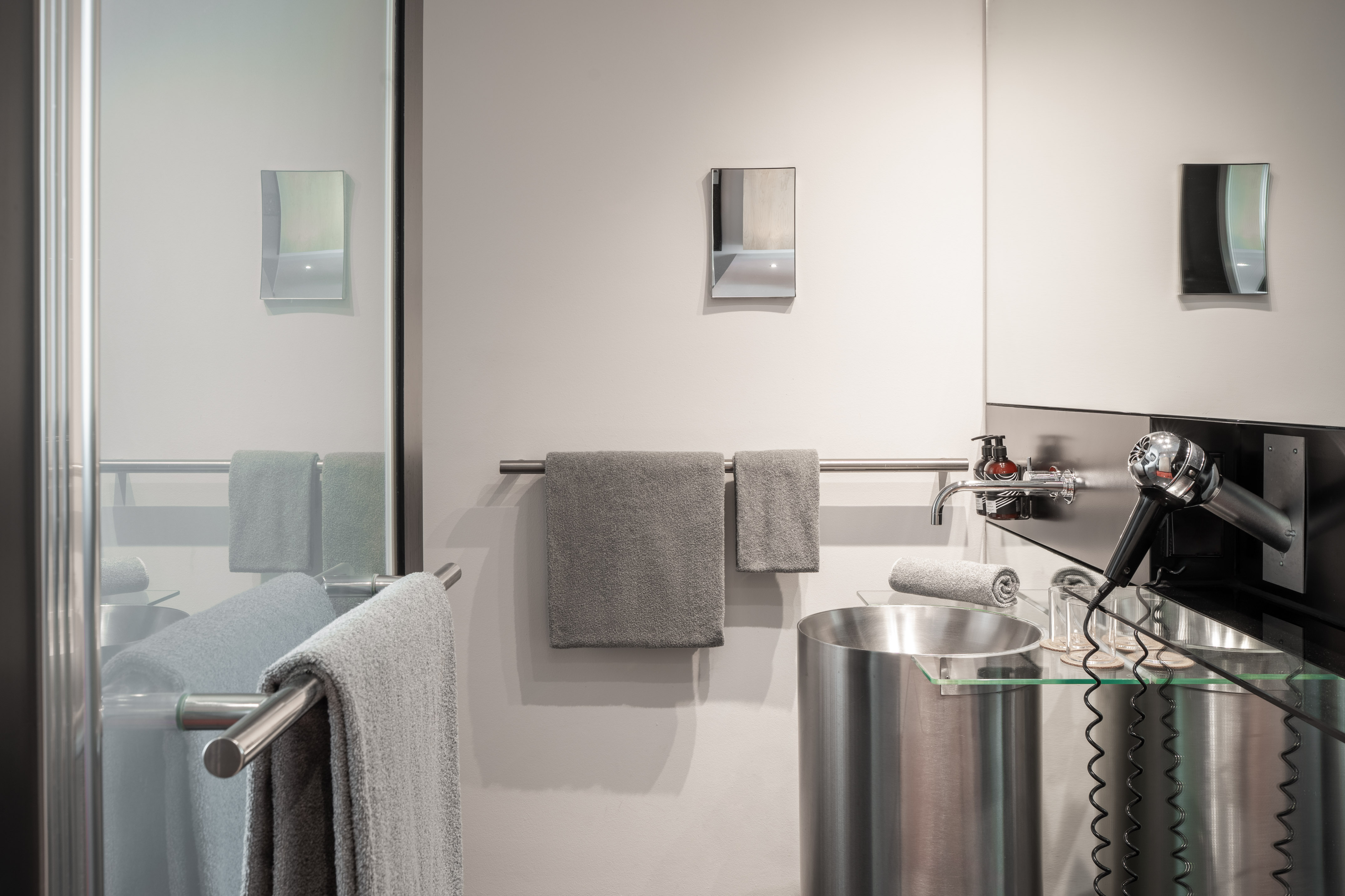 Modern bathroom with stainless steel sink, grey towels, and wall-mounted hairdryer.