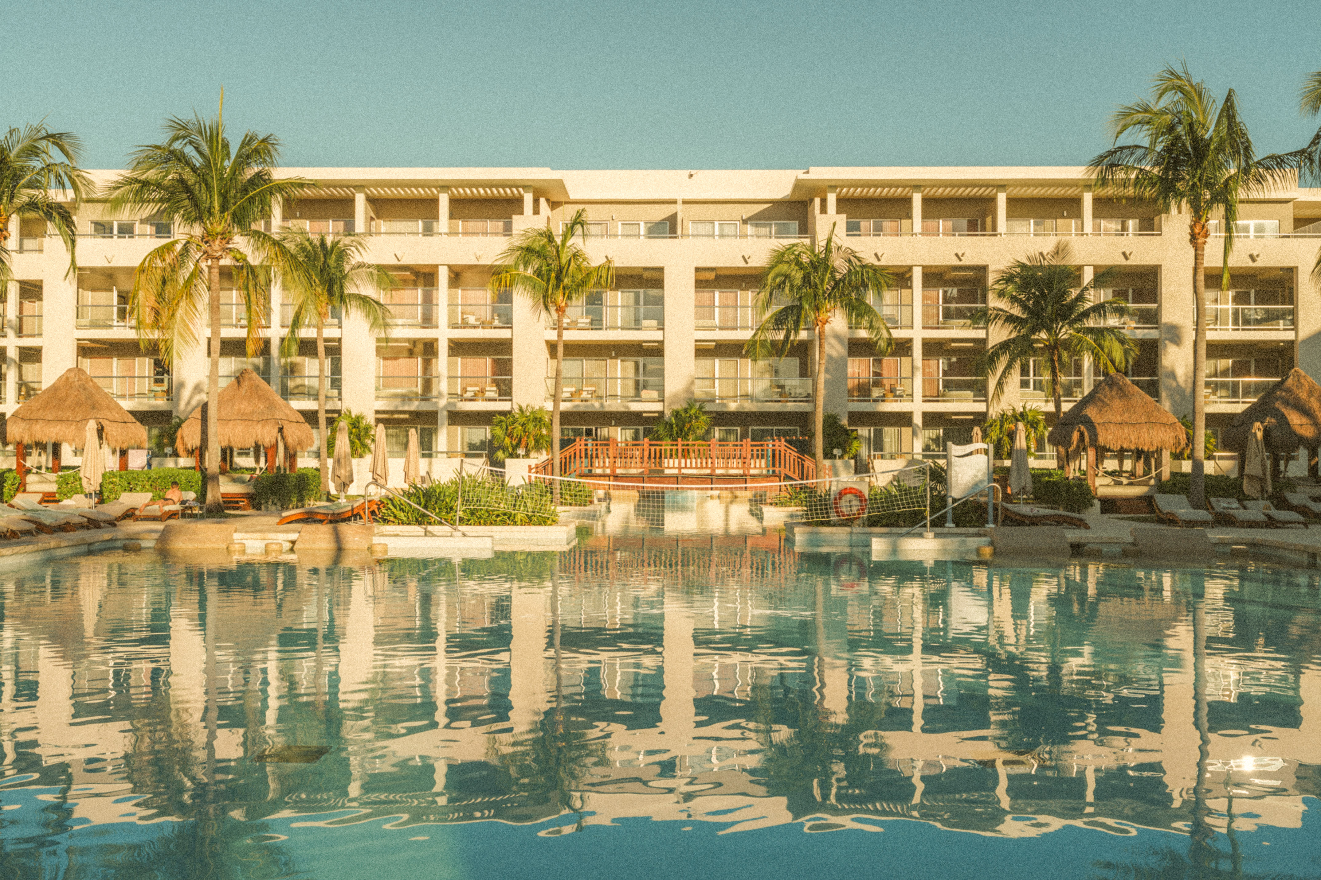 Tropical resort hotel with large pool, palm trees, balconies.