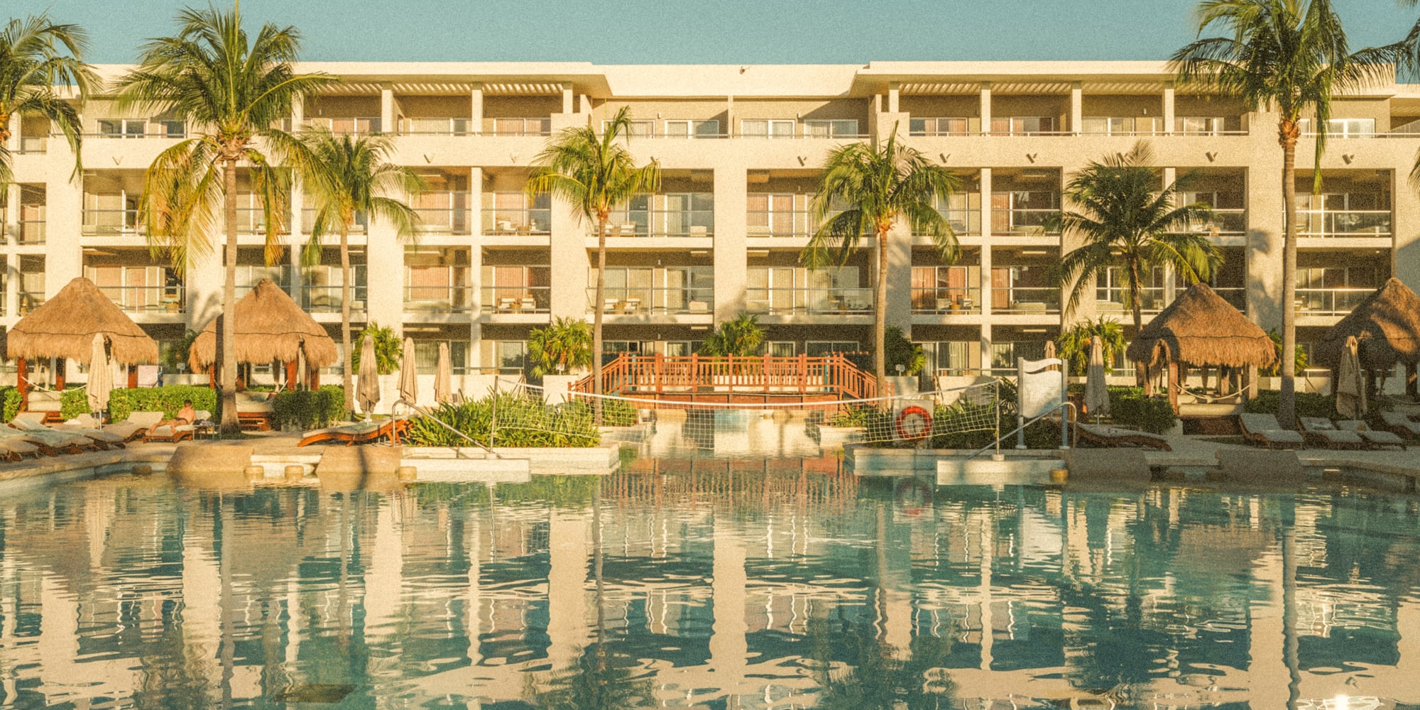 Tropical resort hotel with large pool, palm trees, balconies.