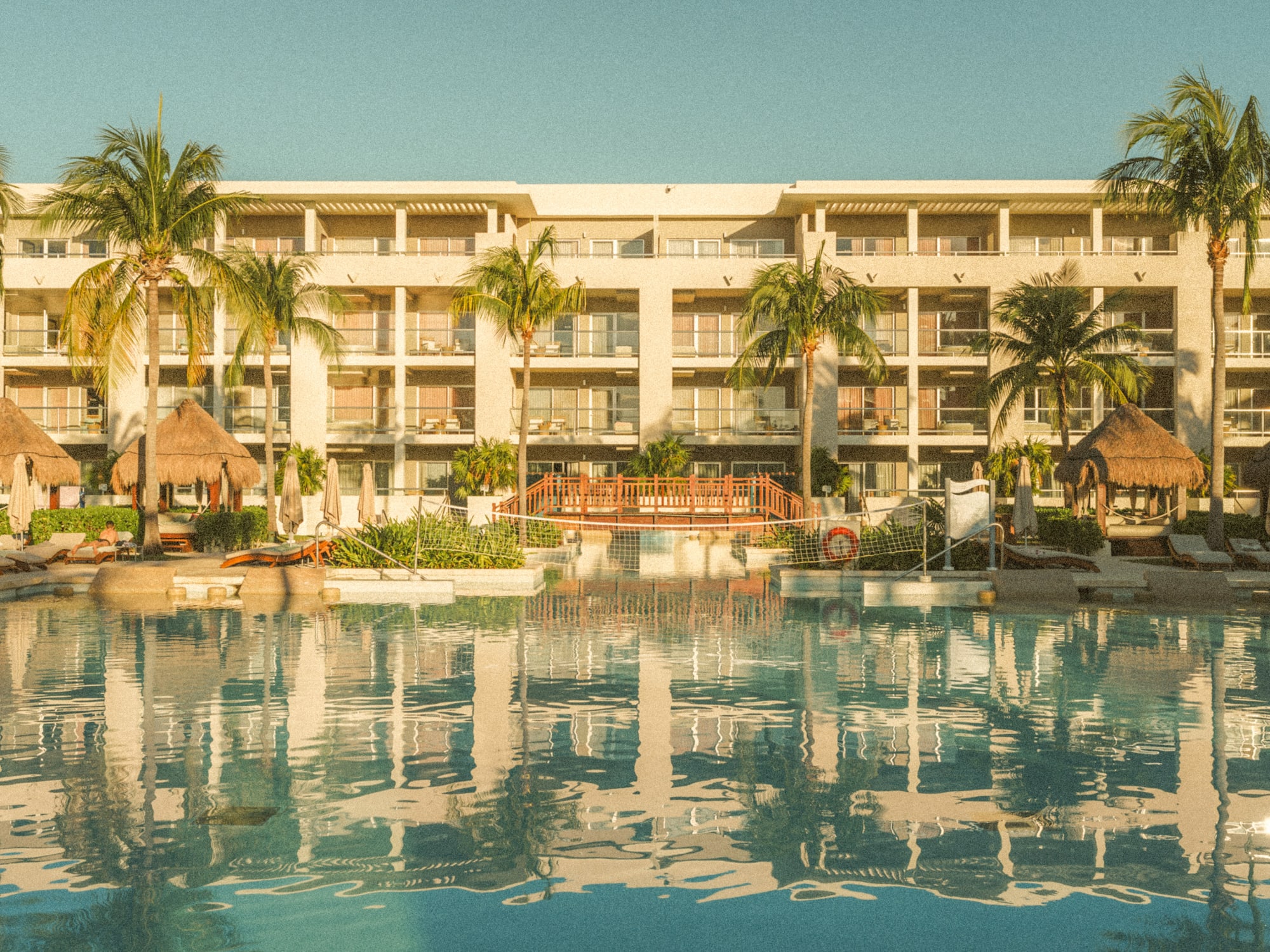 Tropical resort hotel with large pool, palm trees, balconies.