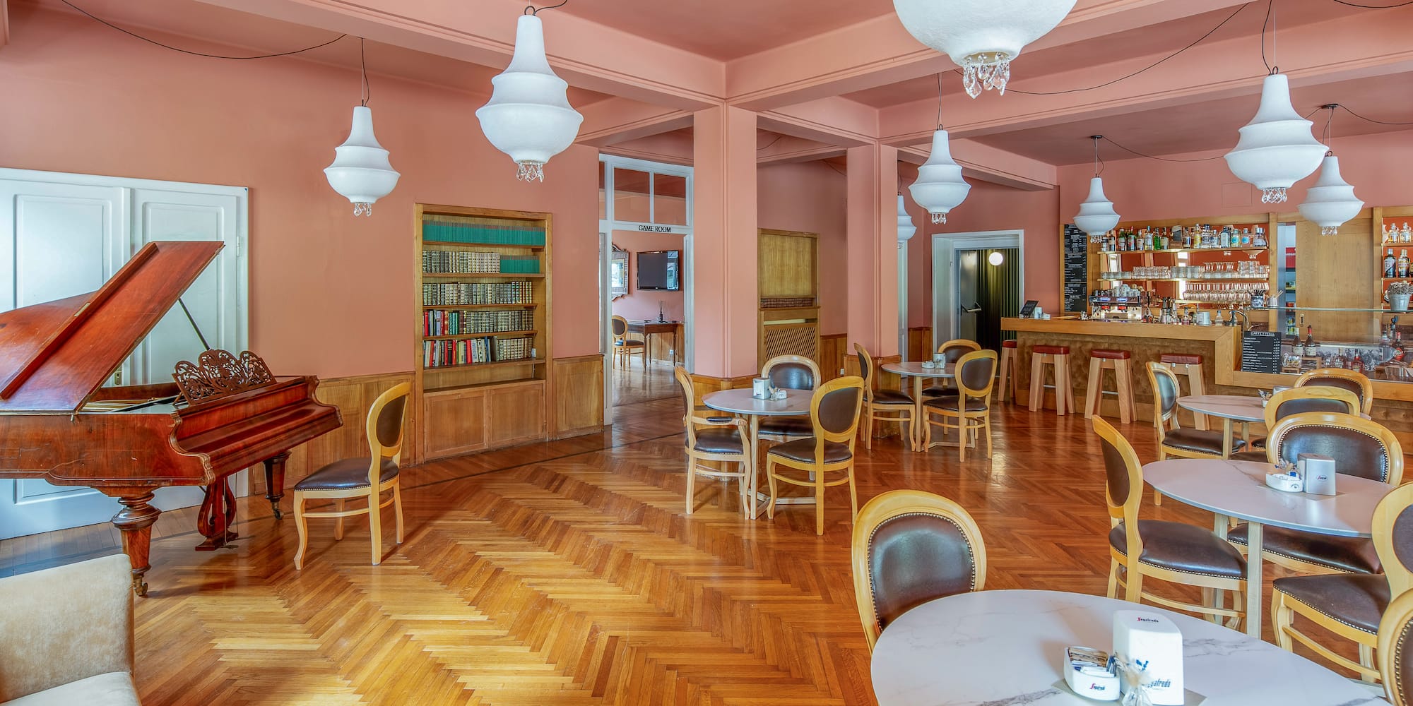 Hotel lounge with grand piano, bar area, peach walls, and parquet floor.