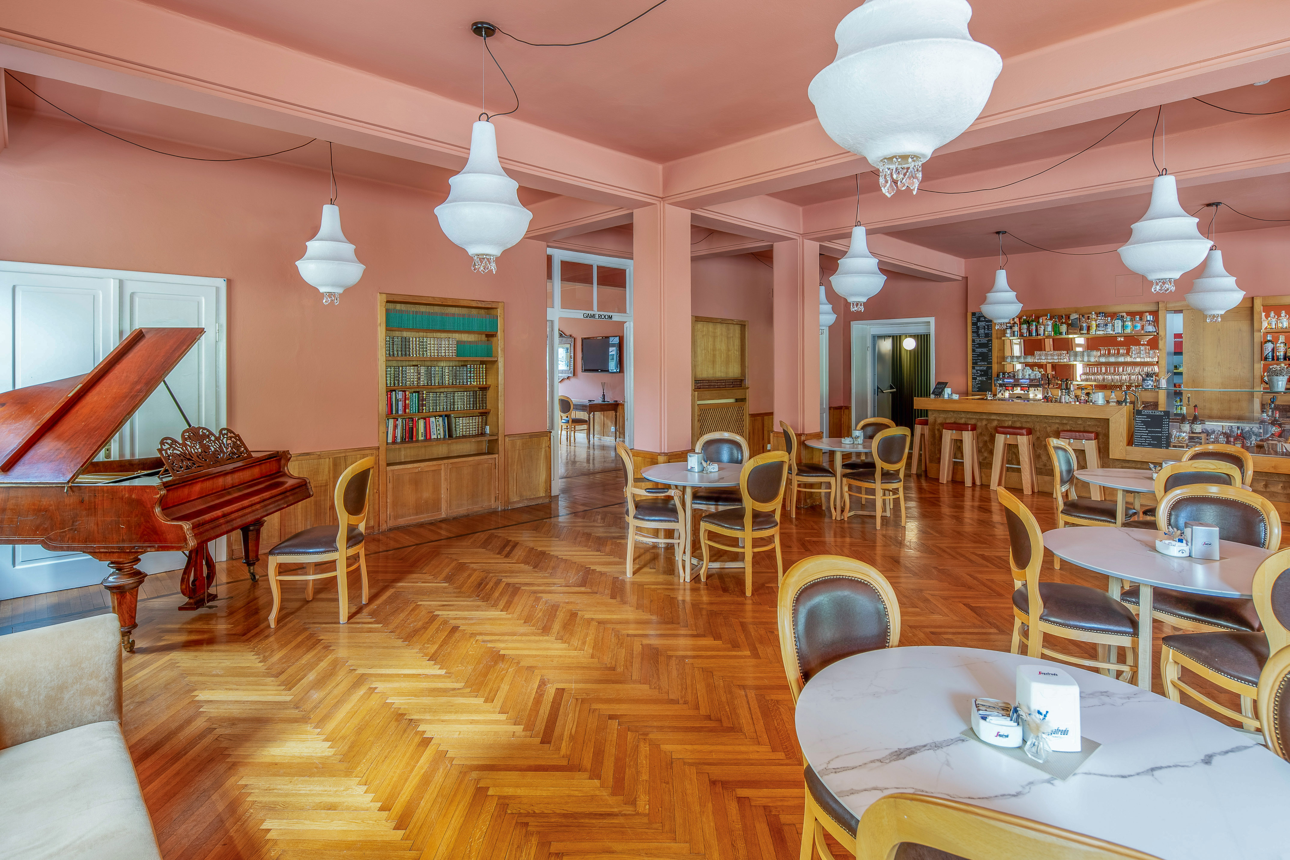 Hotel lounge with grand piano, bar area, peach walls, and parquet floor.