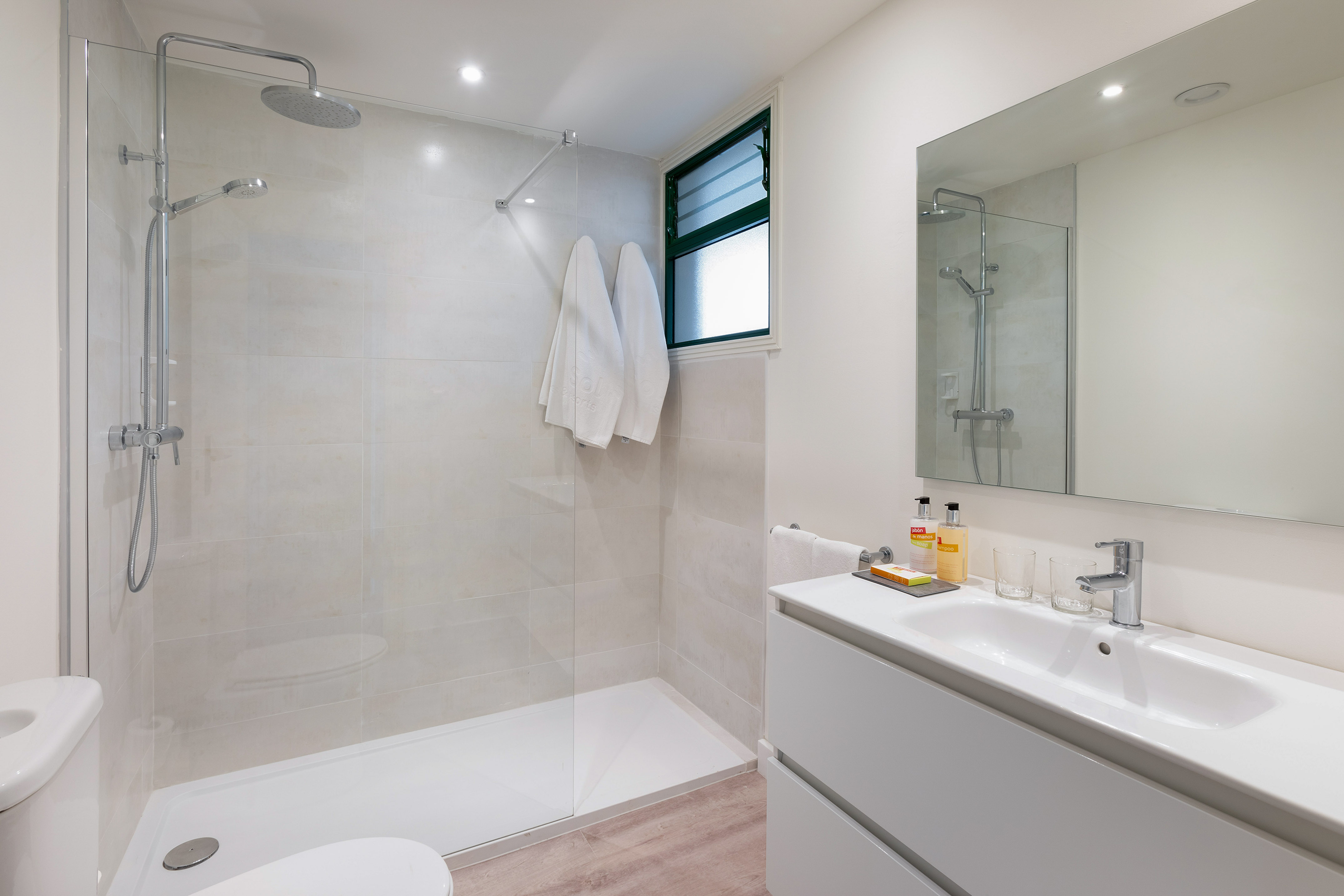 Modern white tiled bathroom with walk-in shower, vanity, mirror, and toilet.