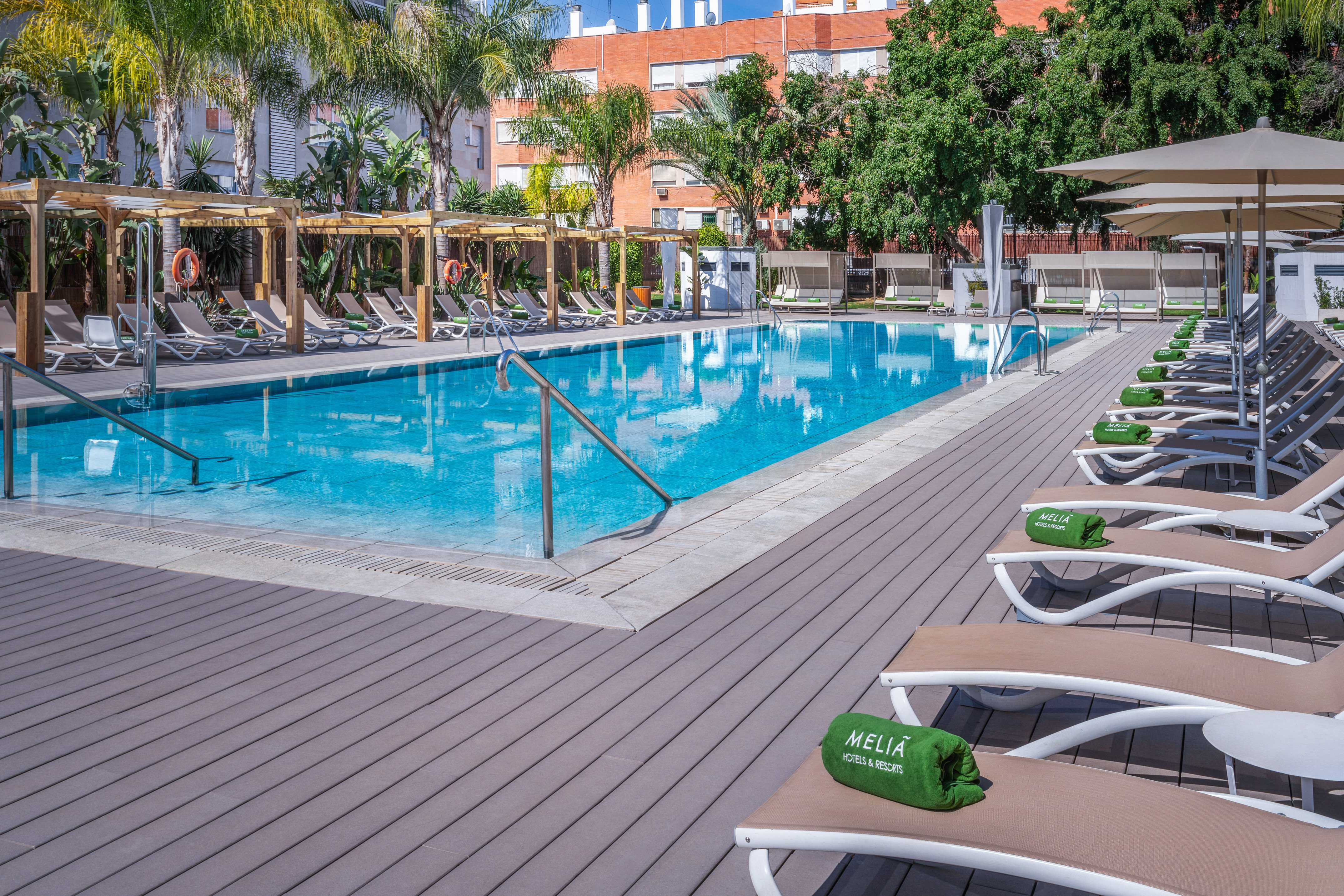 Melia resort pool with sunbeds, palm trees, and wooden deck.