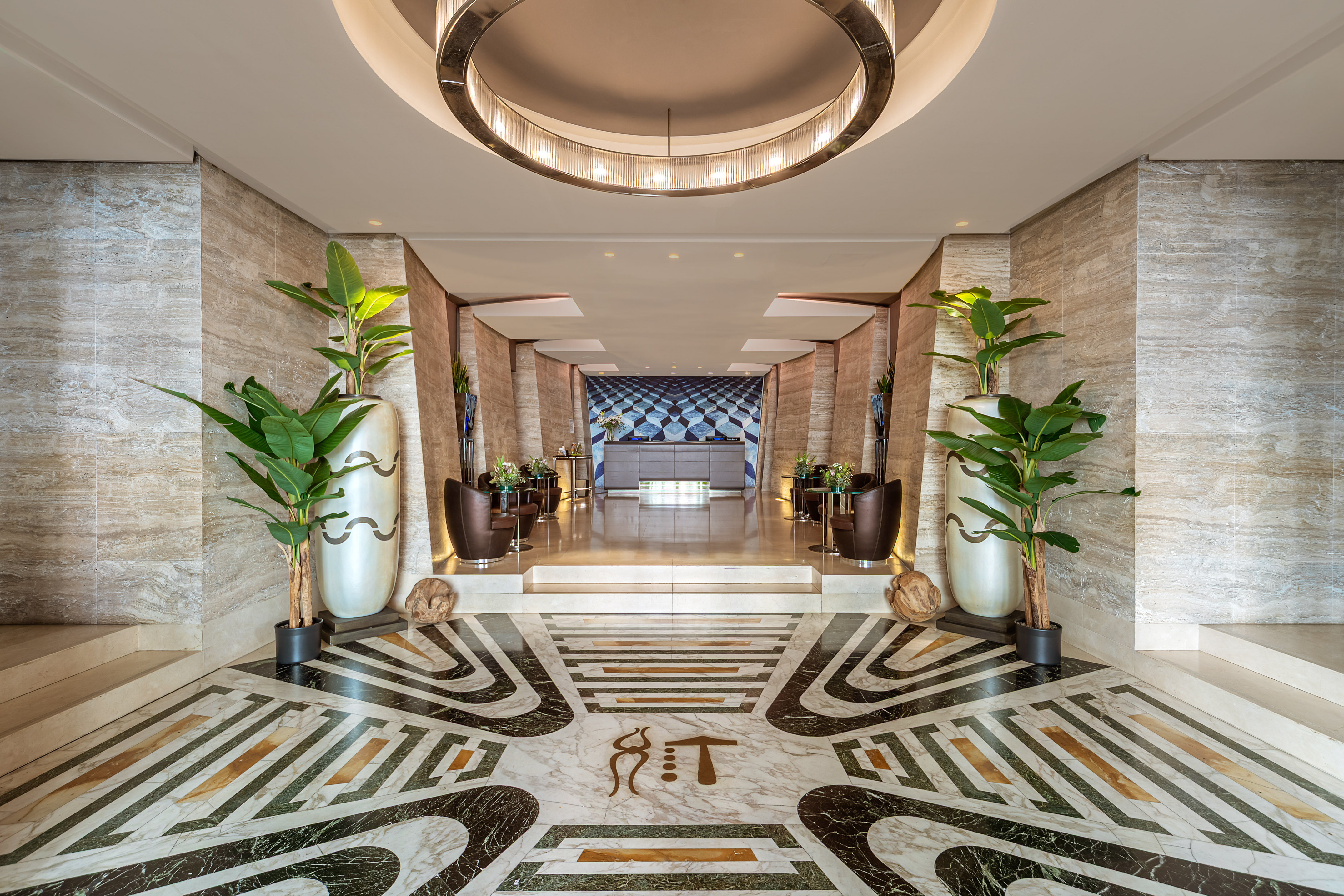 Elegant hotel lobby with ornate marble floor, reception desk, and large plants.