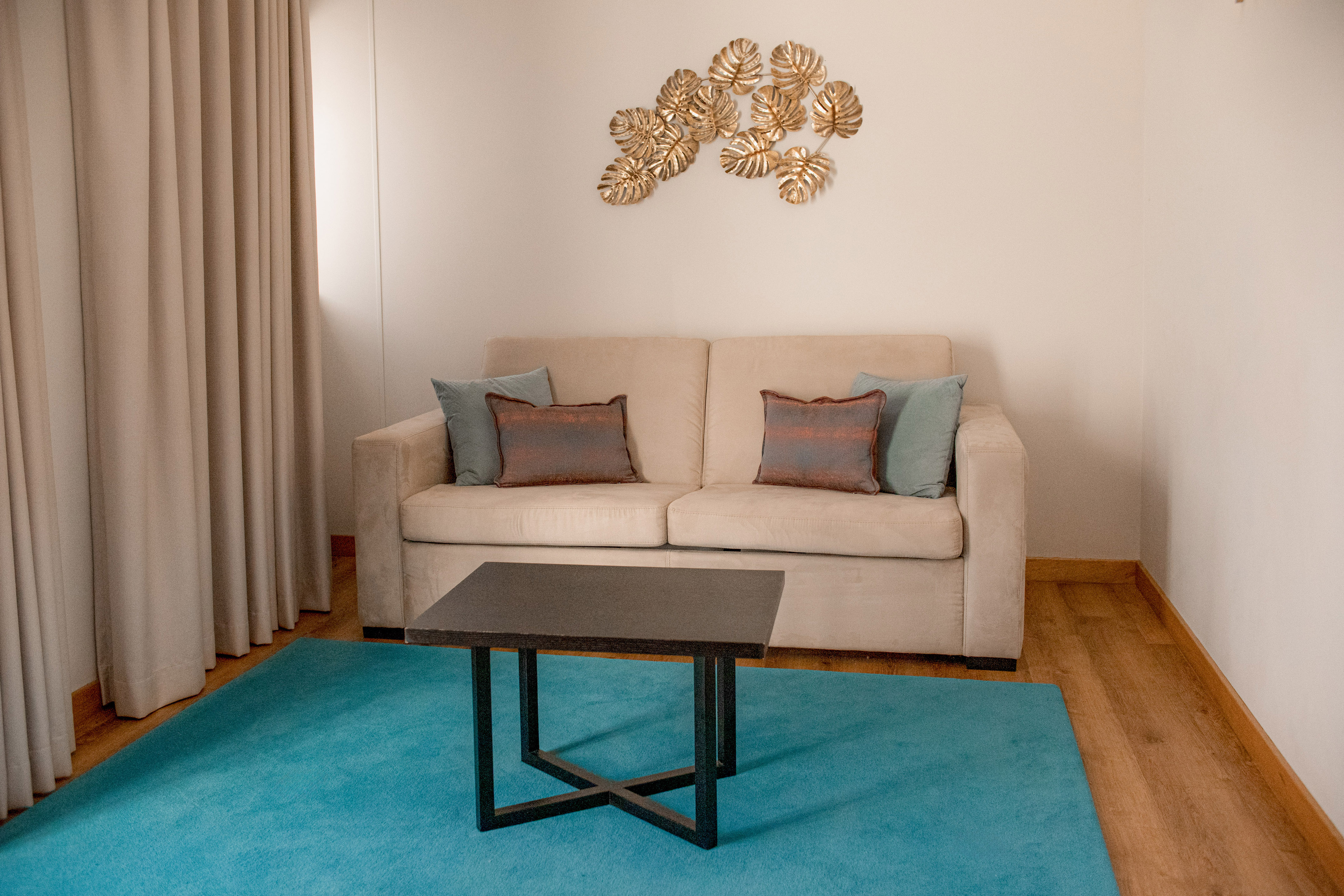 Beige sofa, black coffee table, teal rug, gold leaf art in modern living room.