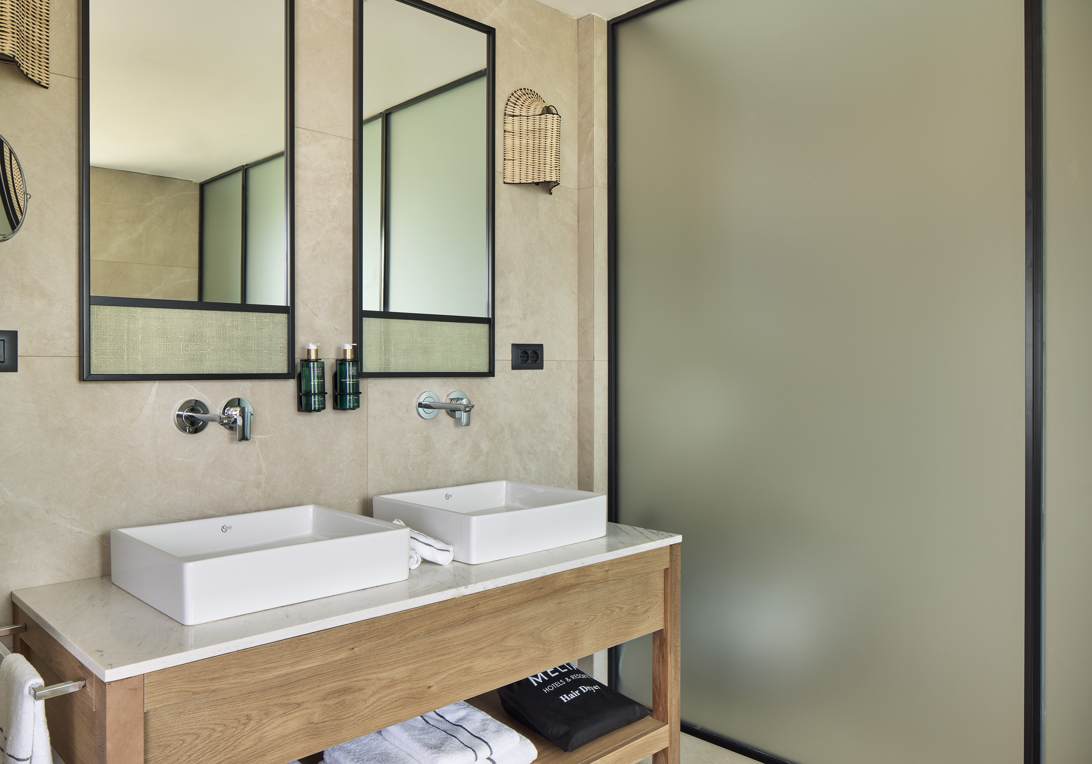 Modern bathroom with double vanity, white sinks, wooden cabinet, and framed mirrors.