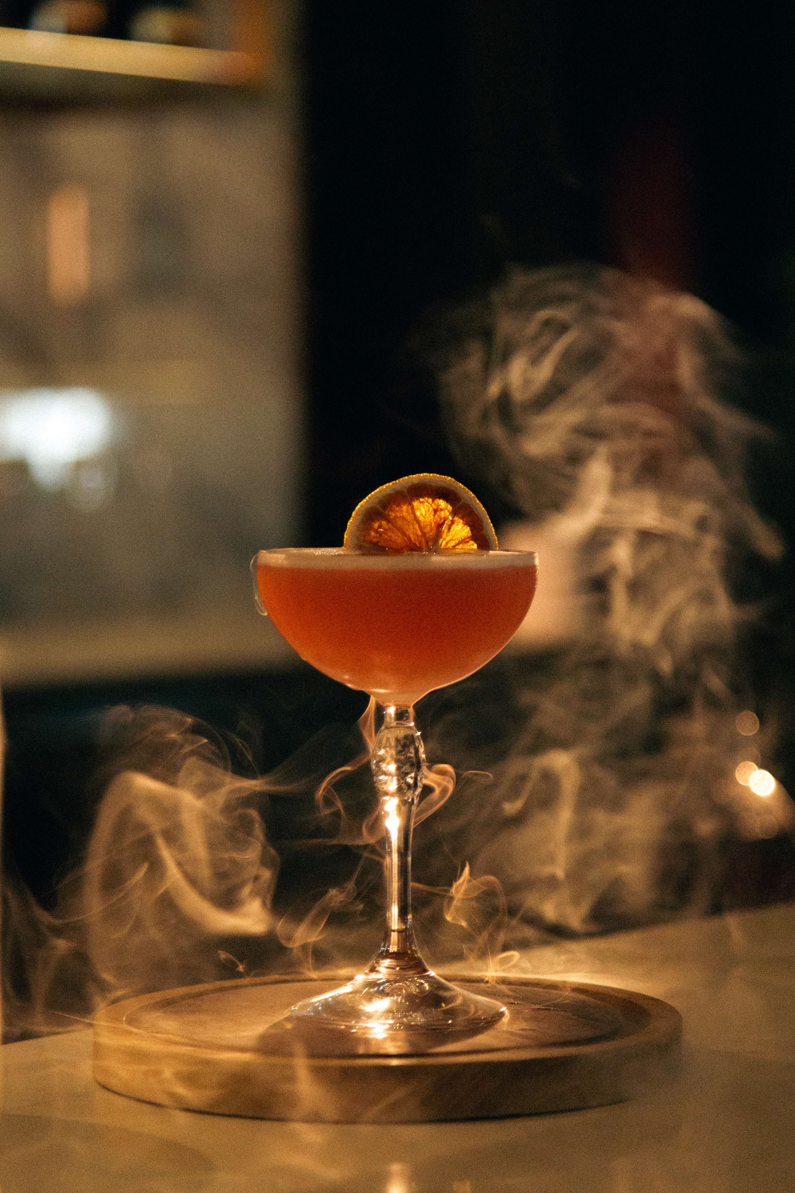 Smoky orange cocktail in coupe glass with dried citrus garnish on a bar.