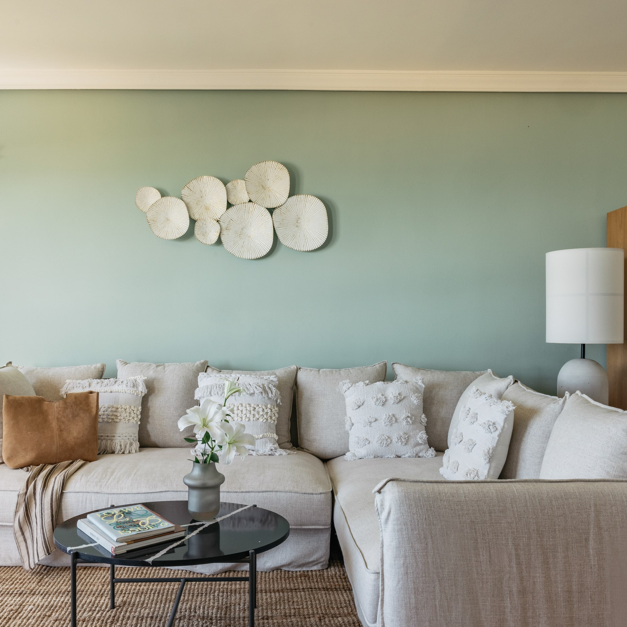 Cozy neutral sectional sofa against sage green wall with textured white decor.