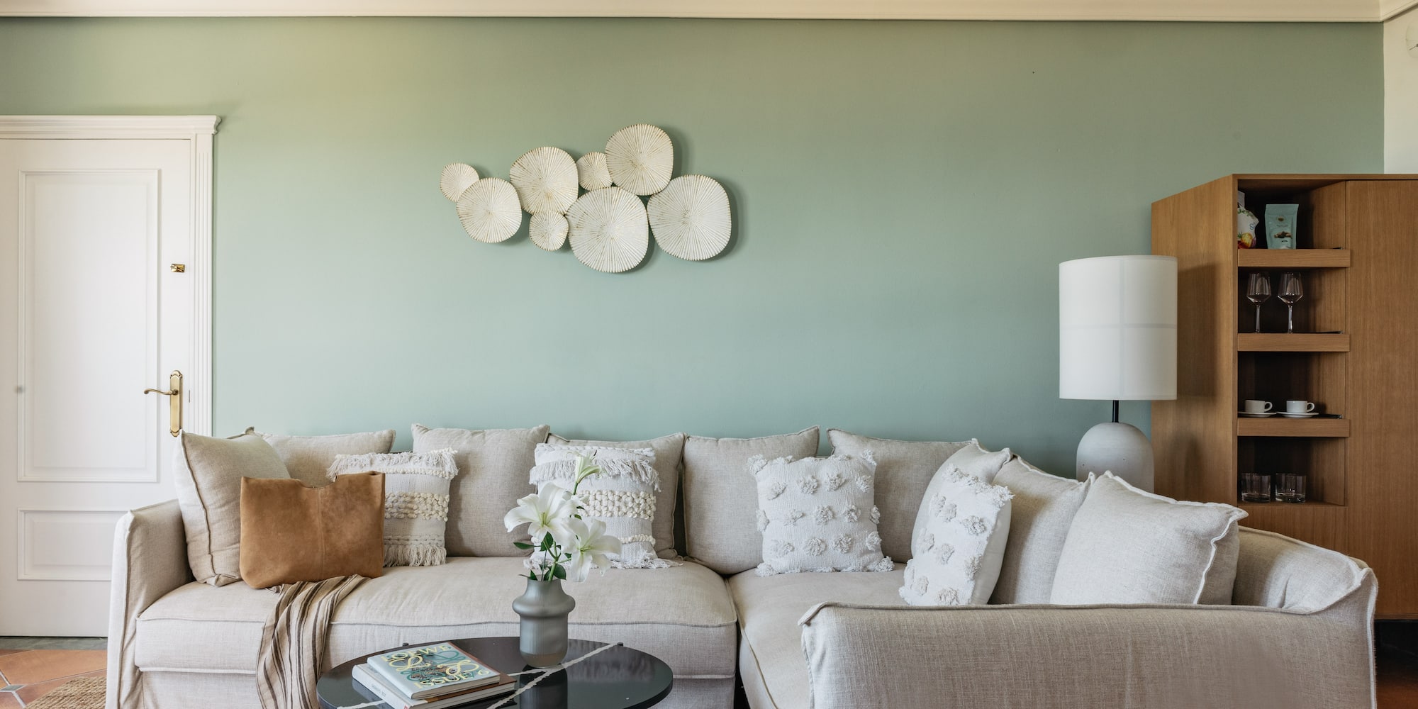 Cozy neutral sectional sofa against sage green wall with textured white decor.