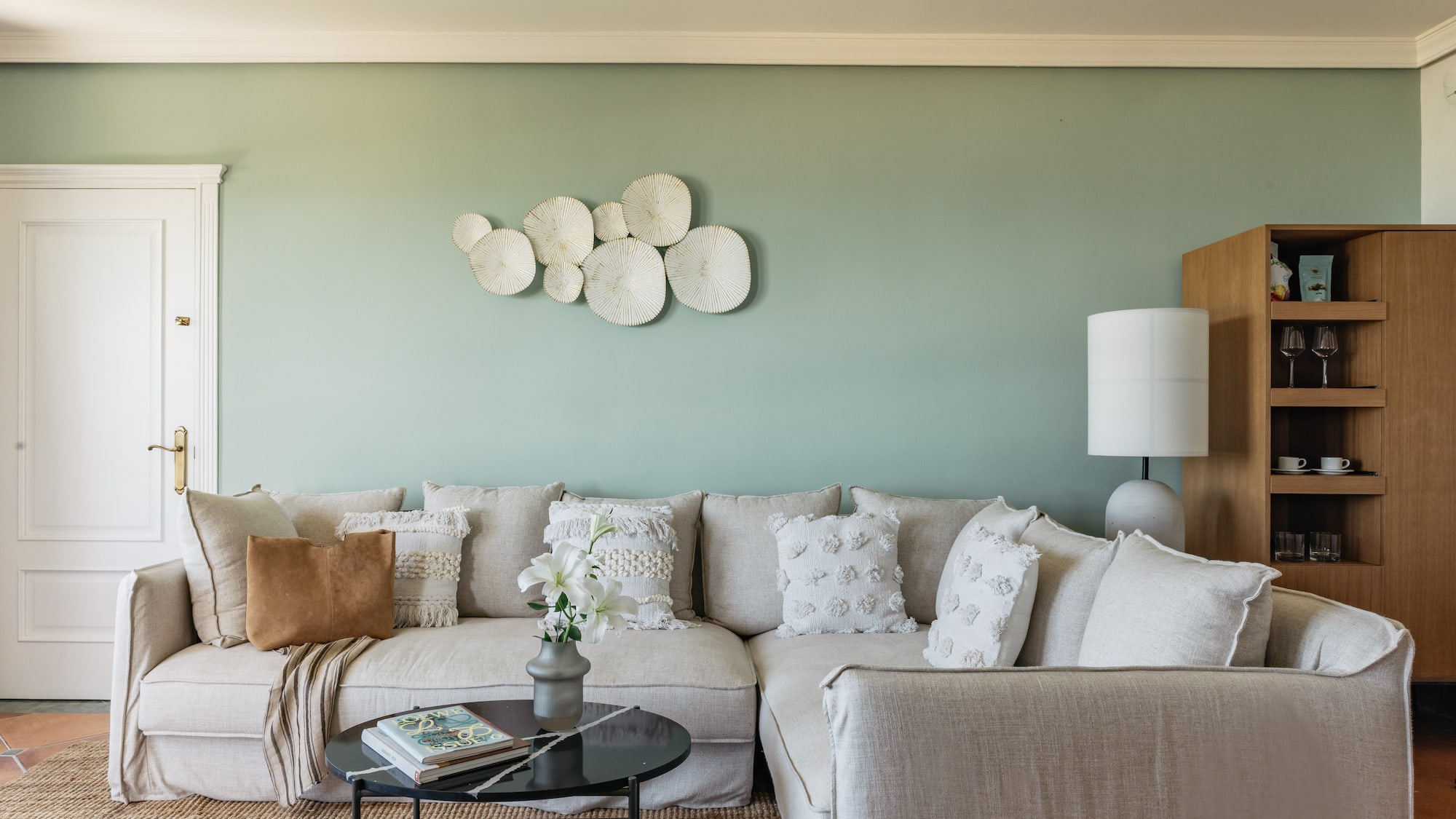 Cozy neutral sectional sofa against sage green wall with textured white decor.