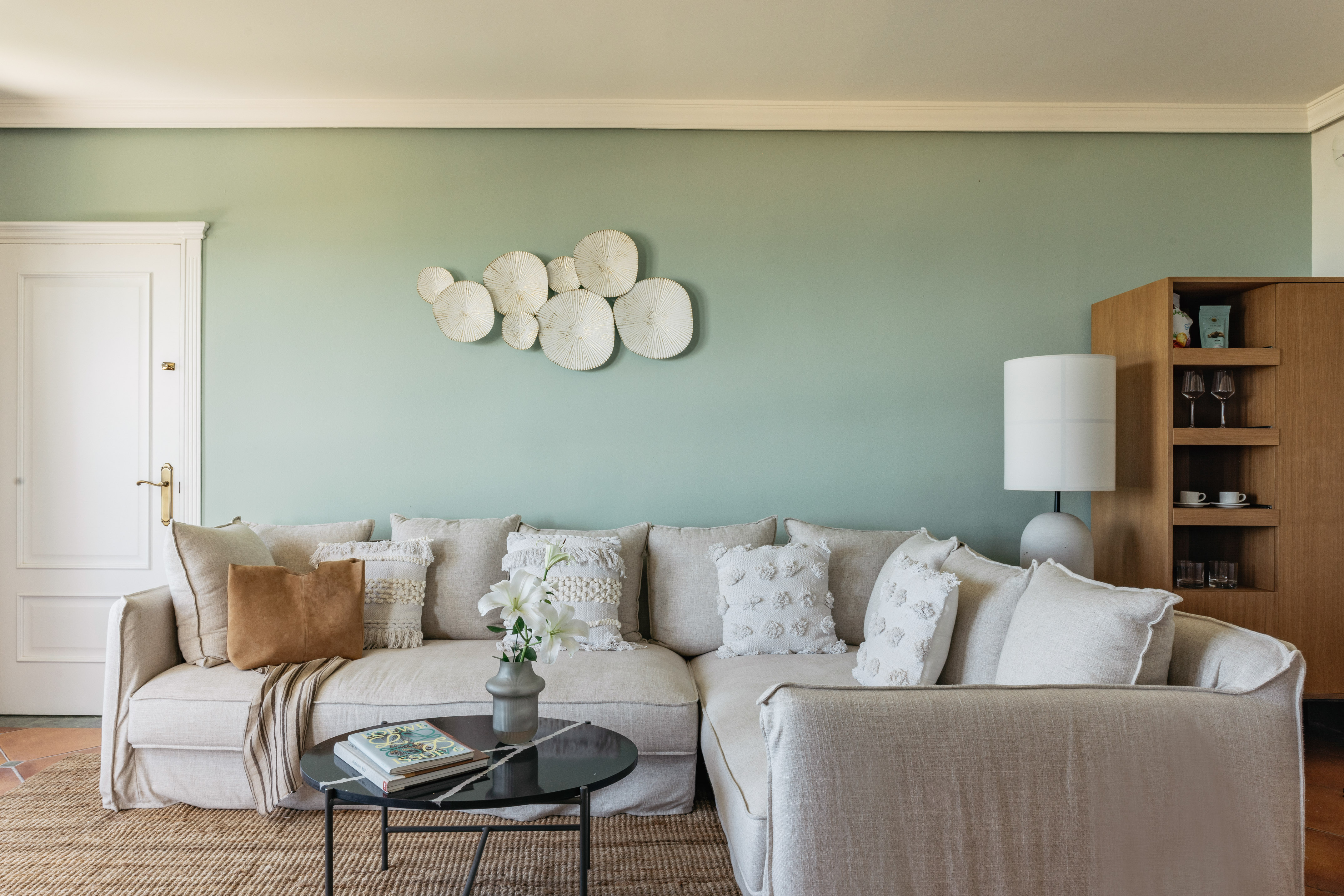 Cozy neutral sectional sofa against sage green wall with textured white decor.