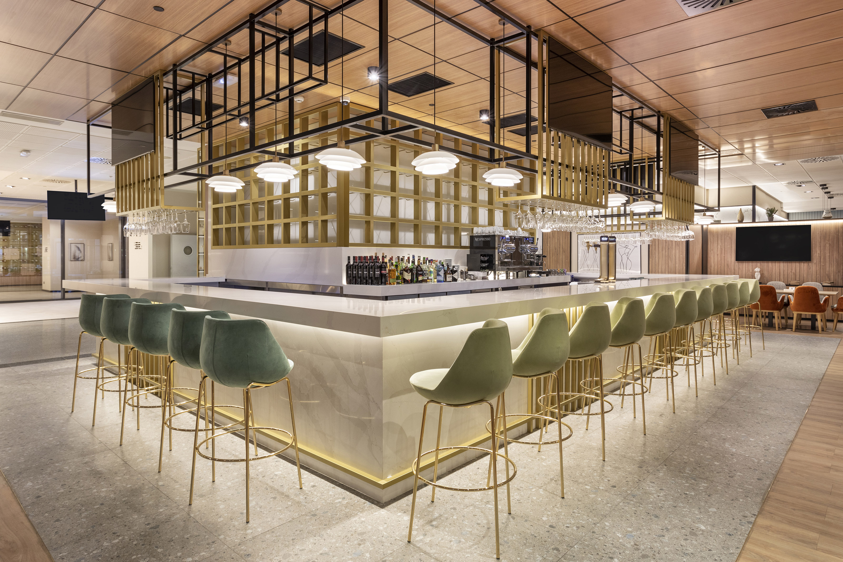 Modern commercial bar with green velvet stools, sleek counter, and gold details.