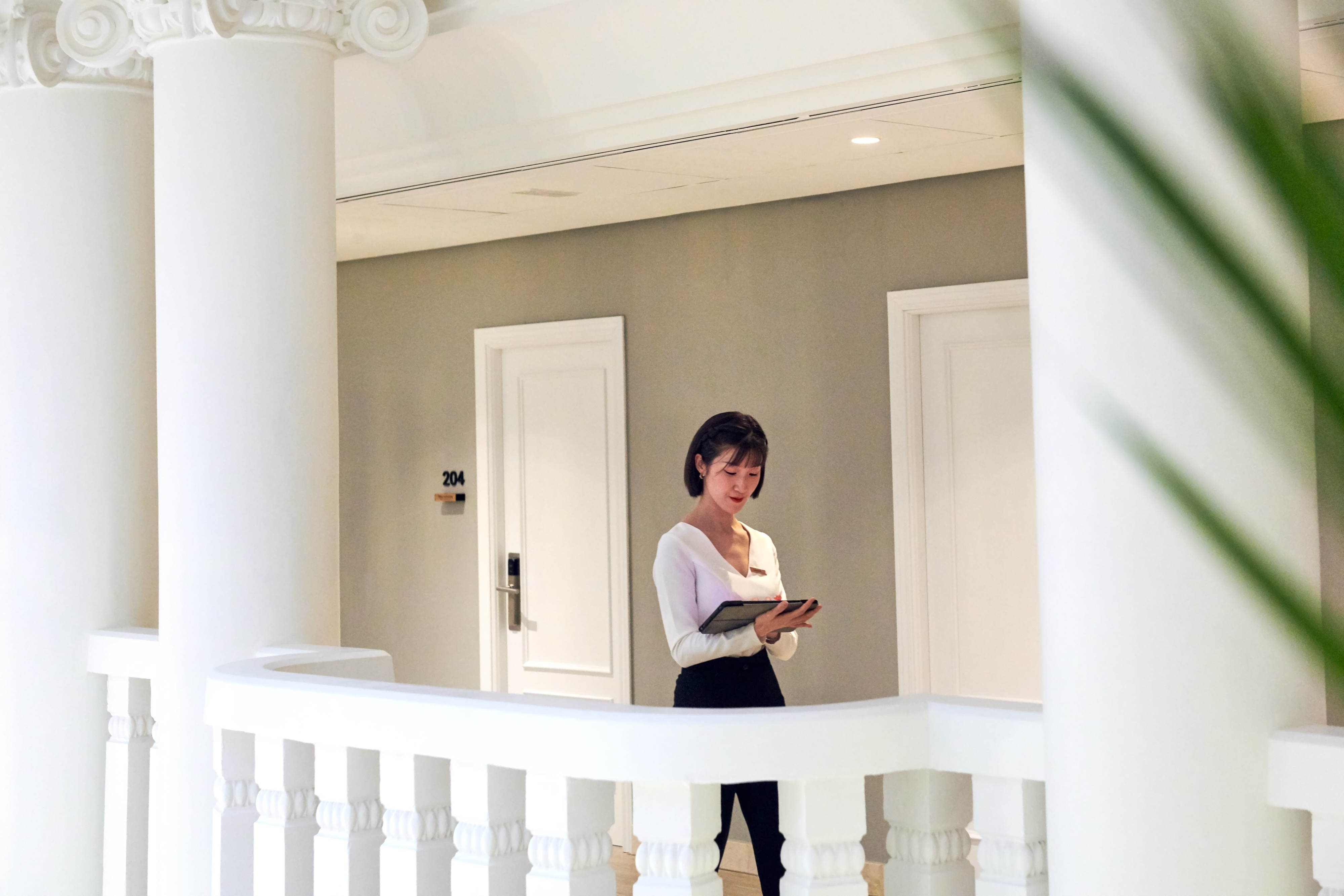 Hotel staff with tablet in elegant hallway, white columns and room 204.