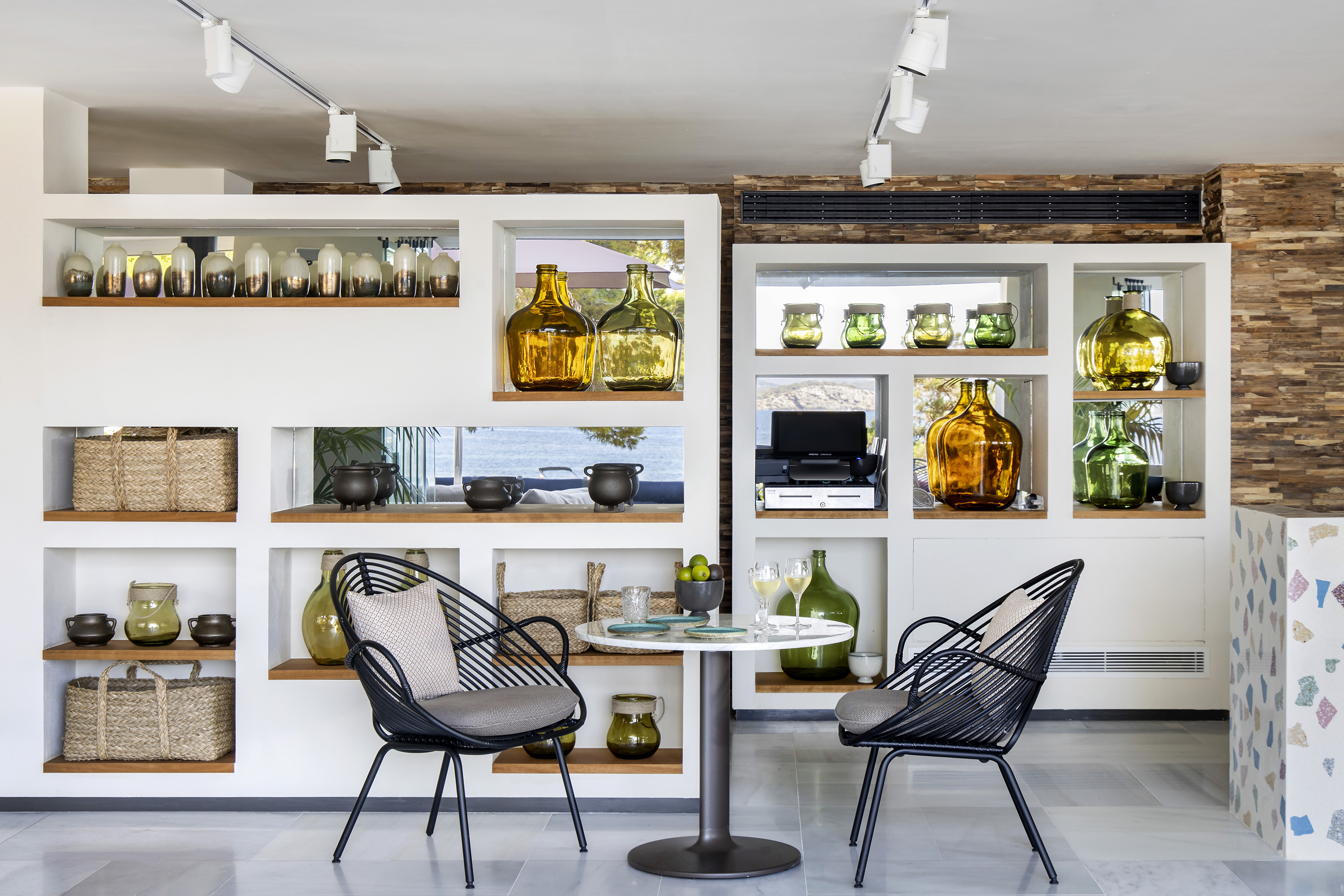 Modern cafe lounge with black chairs, table, decorative bottles, sea view.