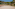 Sandy outdoor beach volleyball court with net, surrounded by green hills and palms.