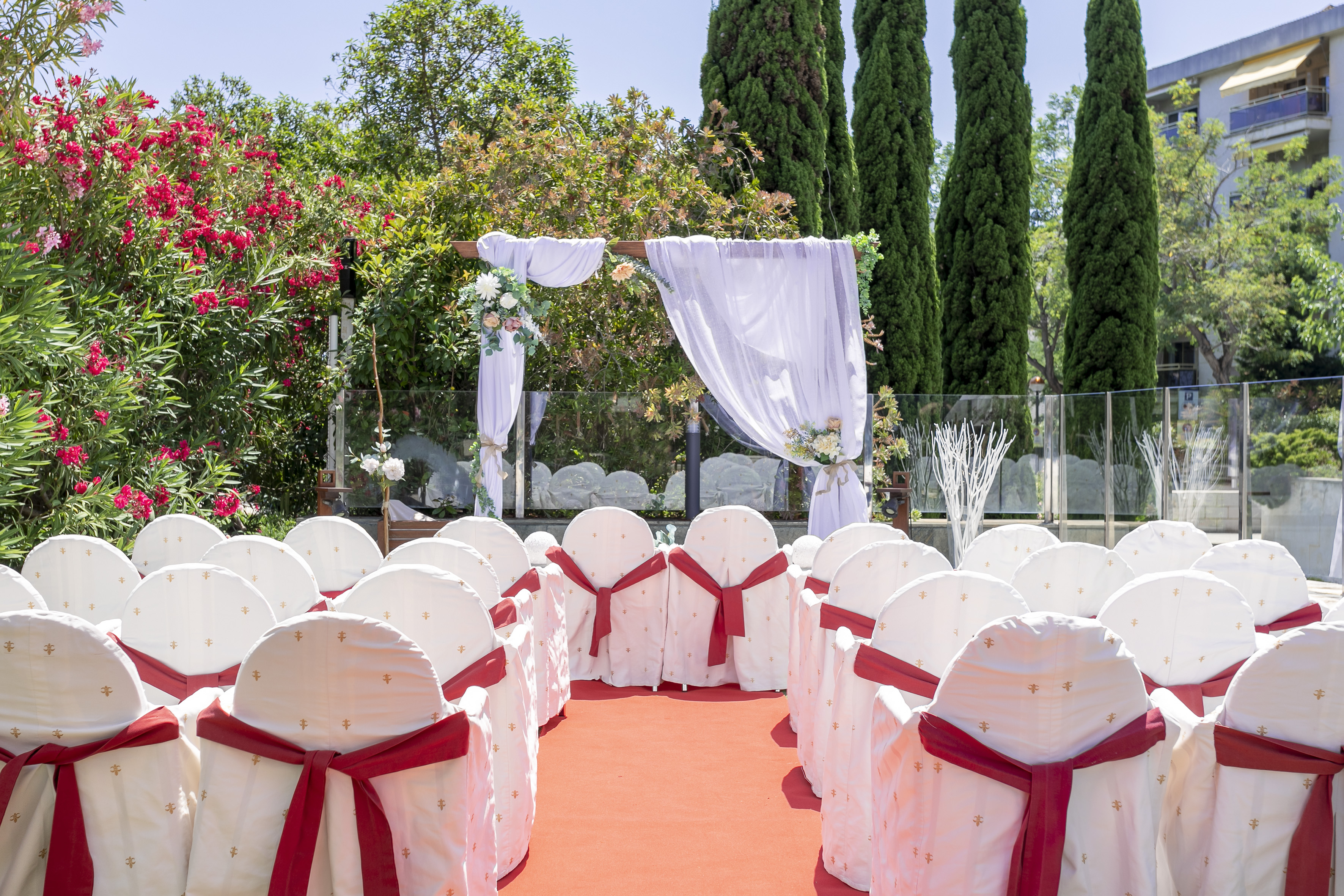 Outdoor wedding ceremony setup: red carpet, white chairs, and floral arch.