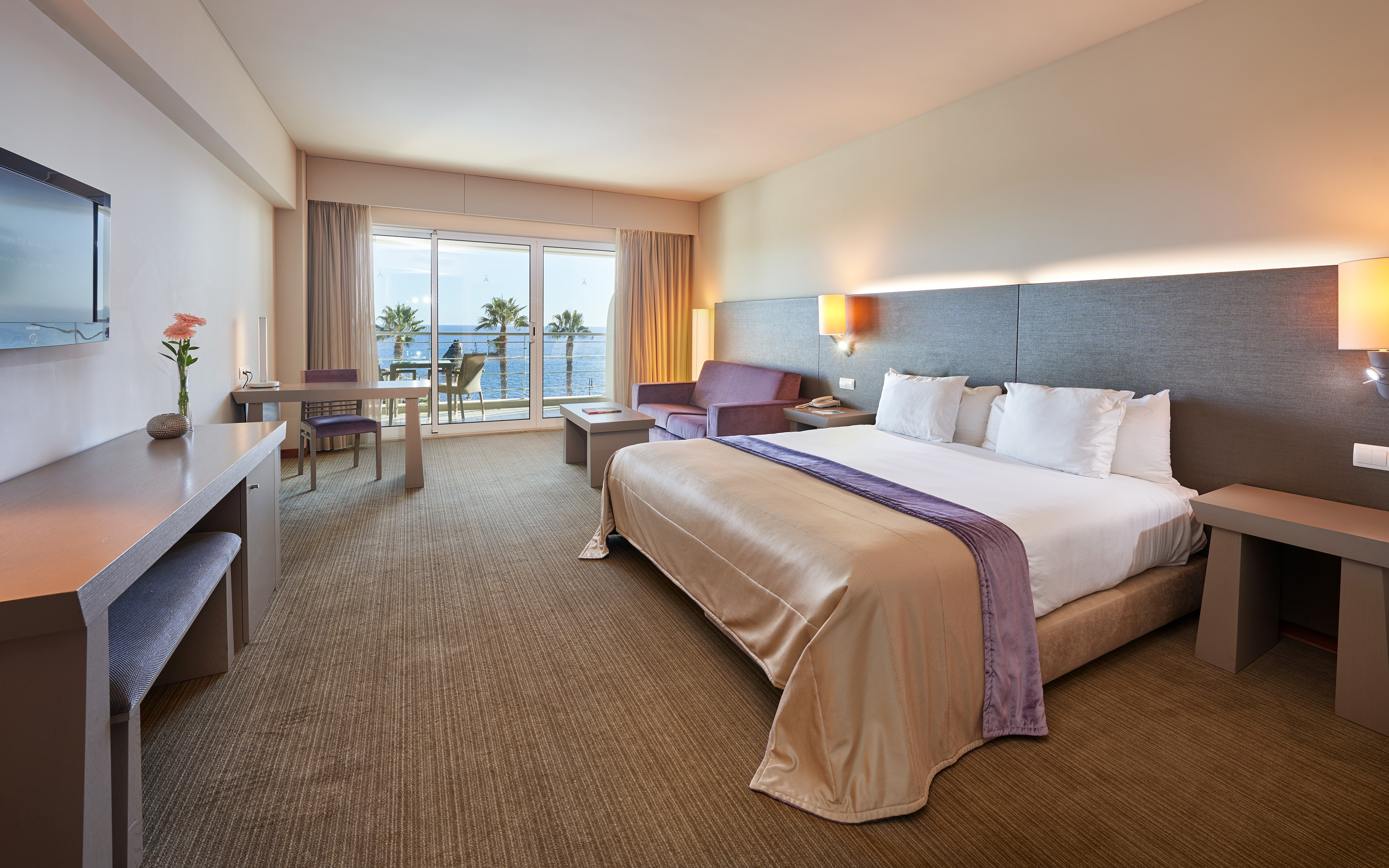 Luxury hotel room with king bed, sofa, and sea view balcony.