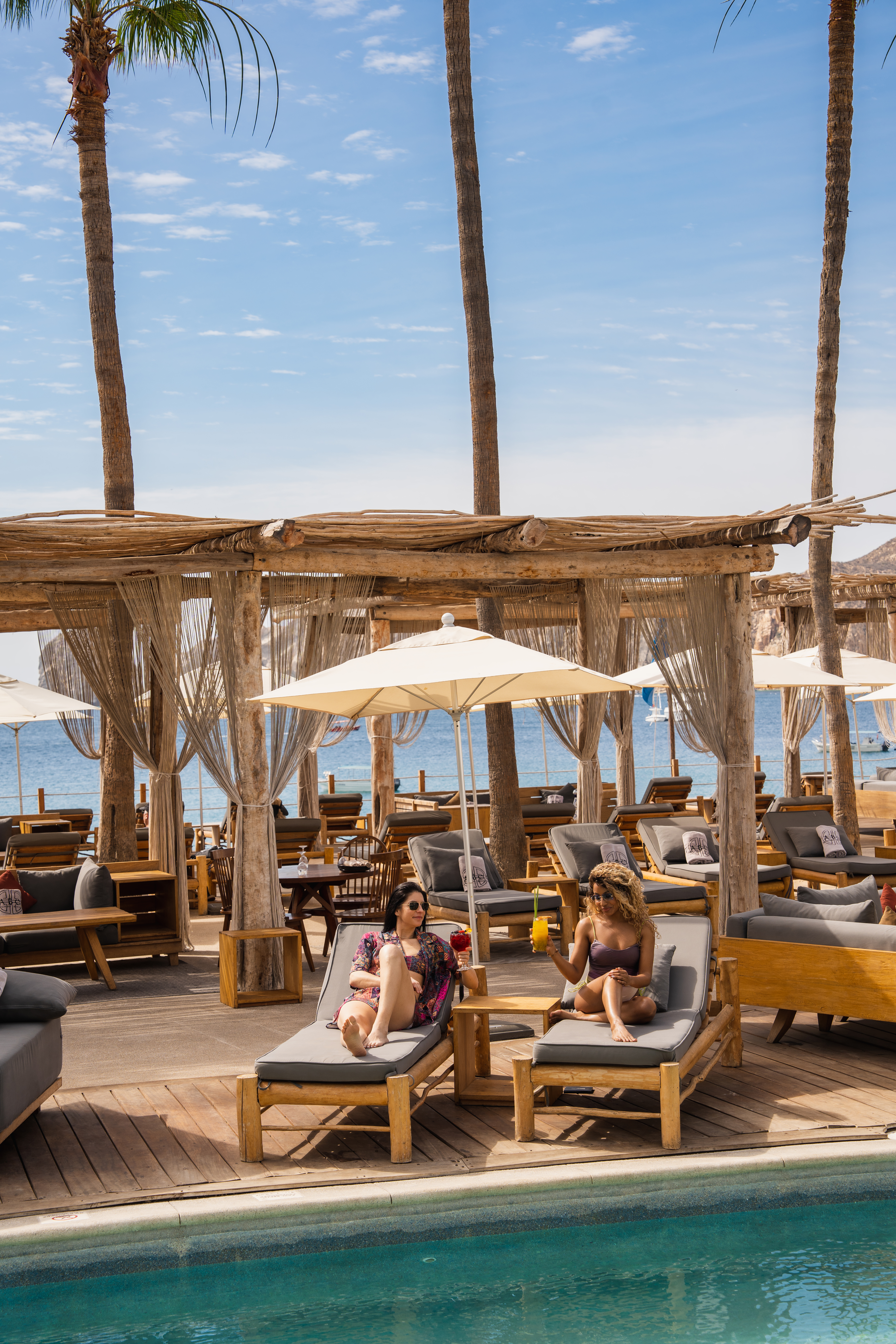 Two women enjoying cocktails by the pool at a beach resort with an ocean view.