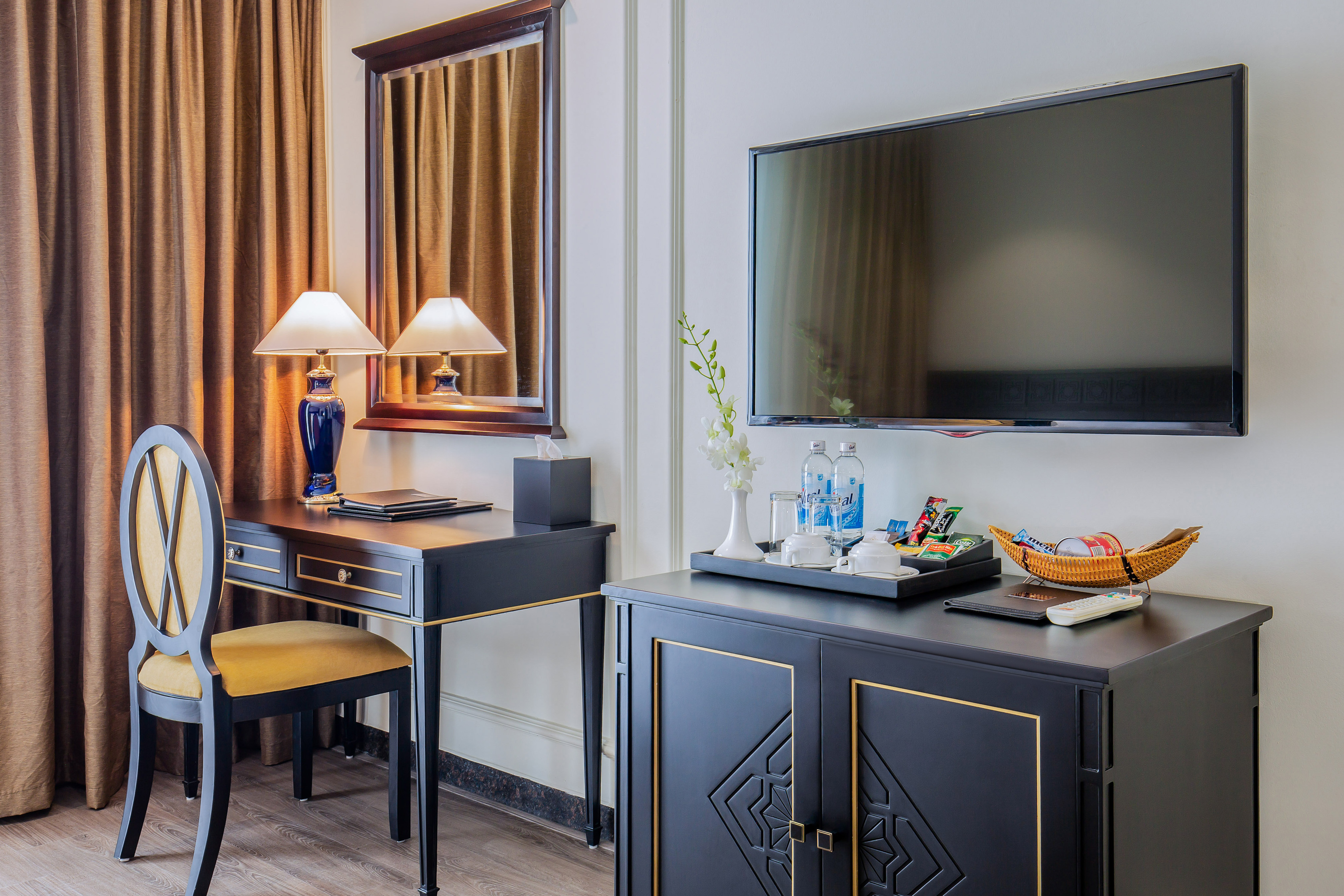 Elegant hotel room: dark desk, chair, wall-mounted TV, refreshment cabinet.