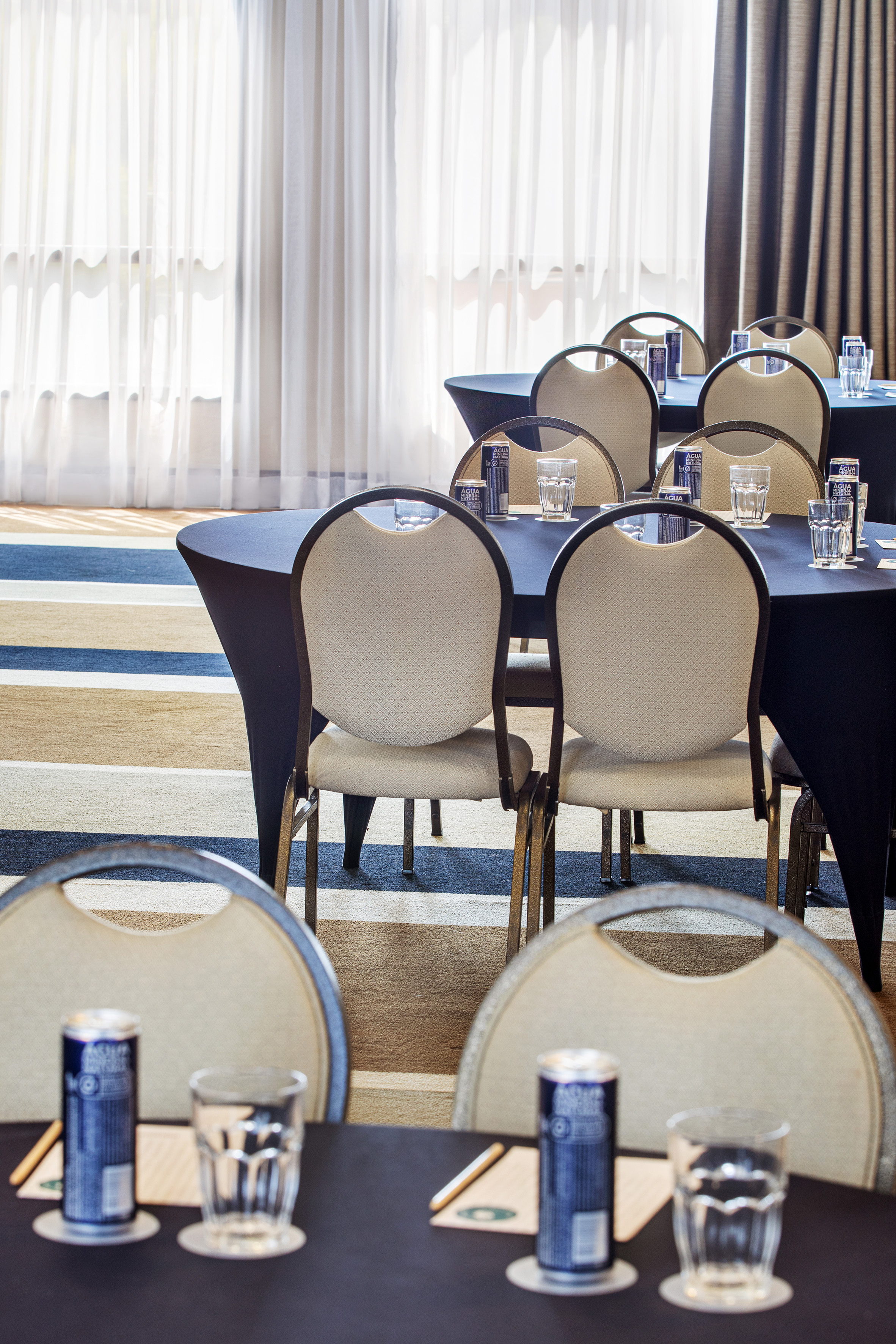 Meeting room with tables, chairs, mineral water, and windows.