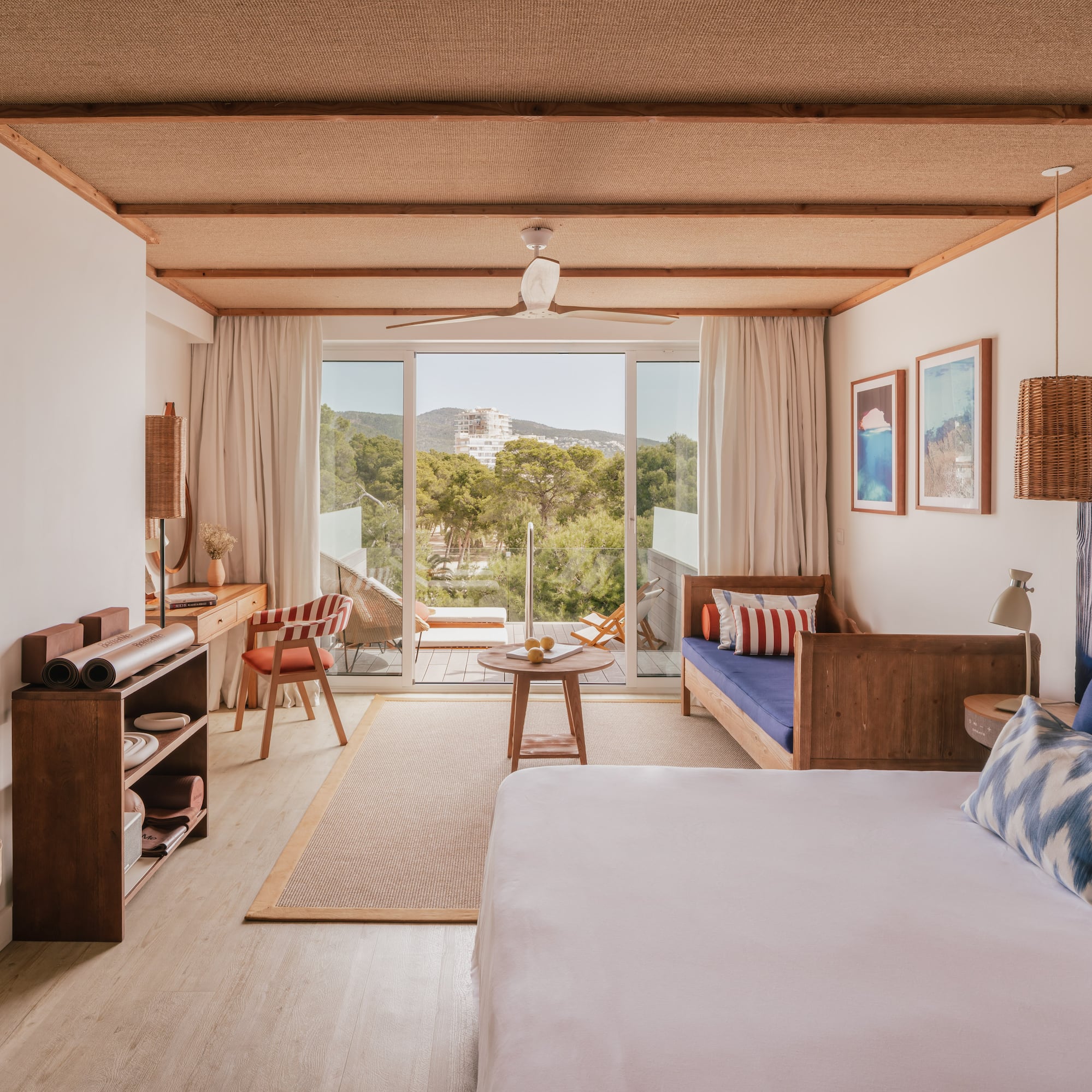Modern resort room with balcony, nature view, woven ceiling, and wood furniture.
