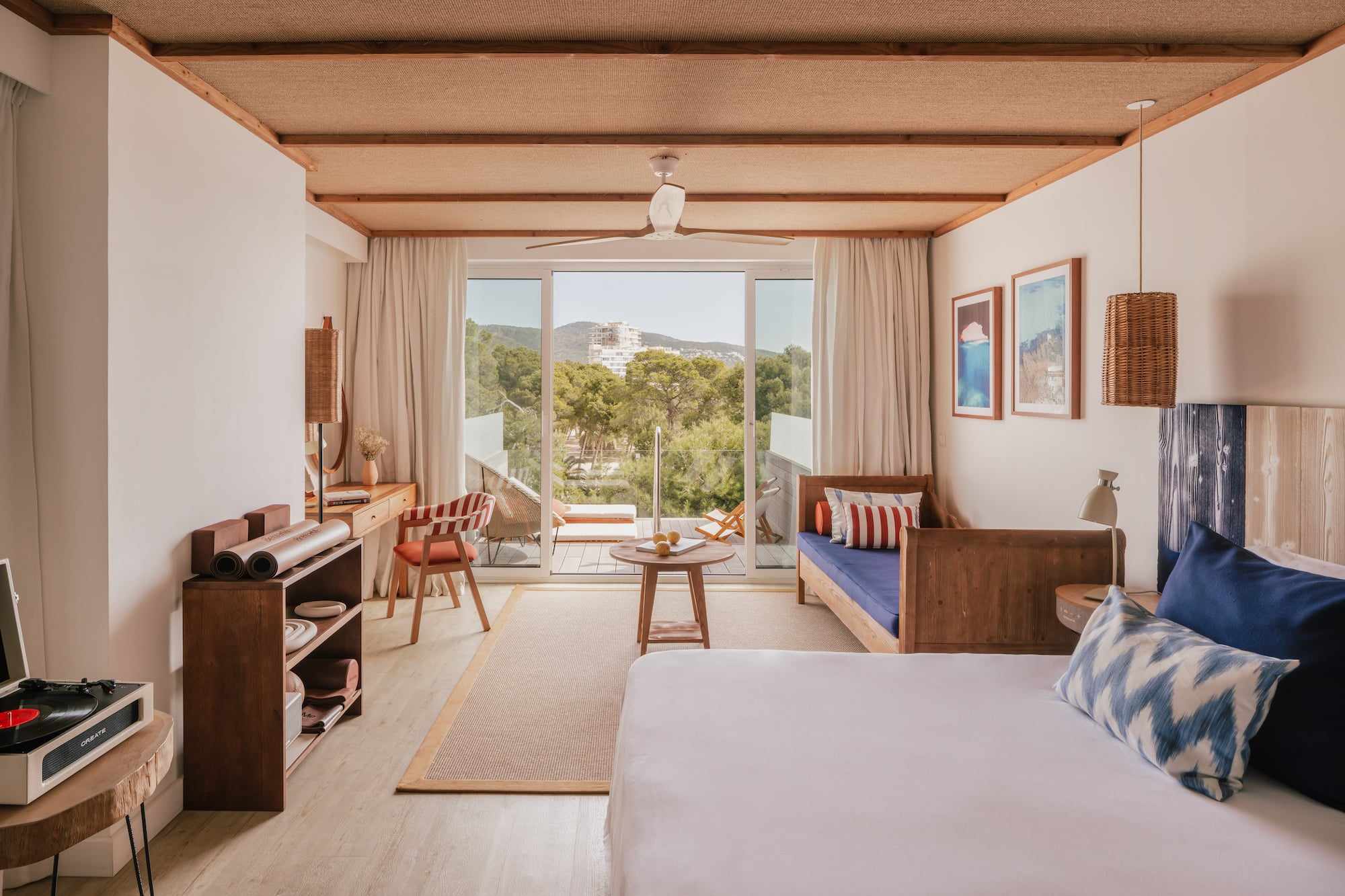 Modern resort room with balcony, nature view, woven ceiling, and wood furniture.