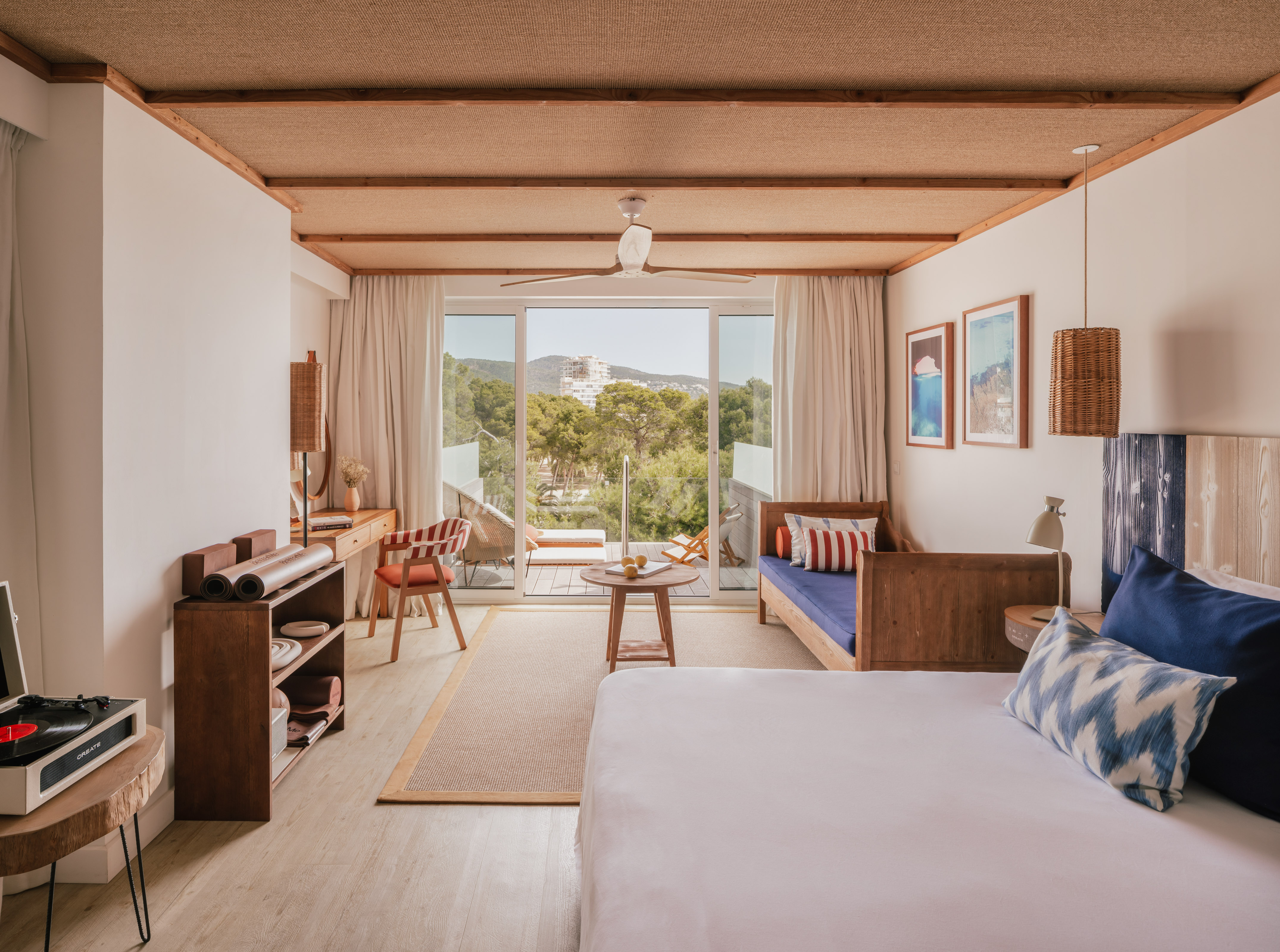 Modern resort room with balcony, nature view, woven ceiling, and wood furniture.
